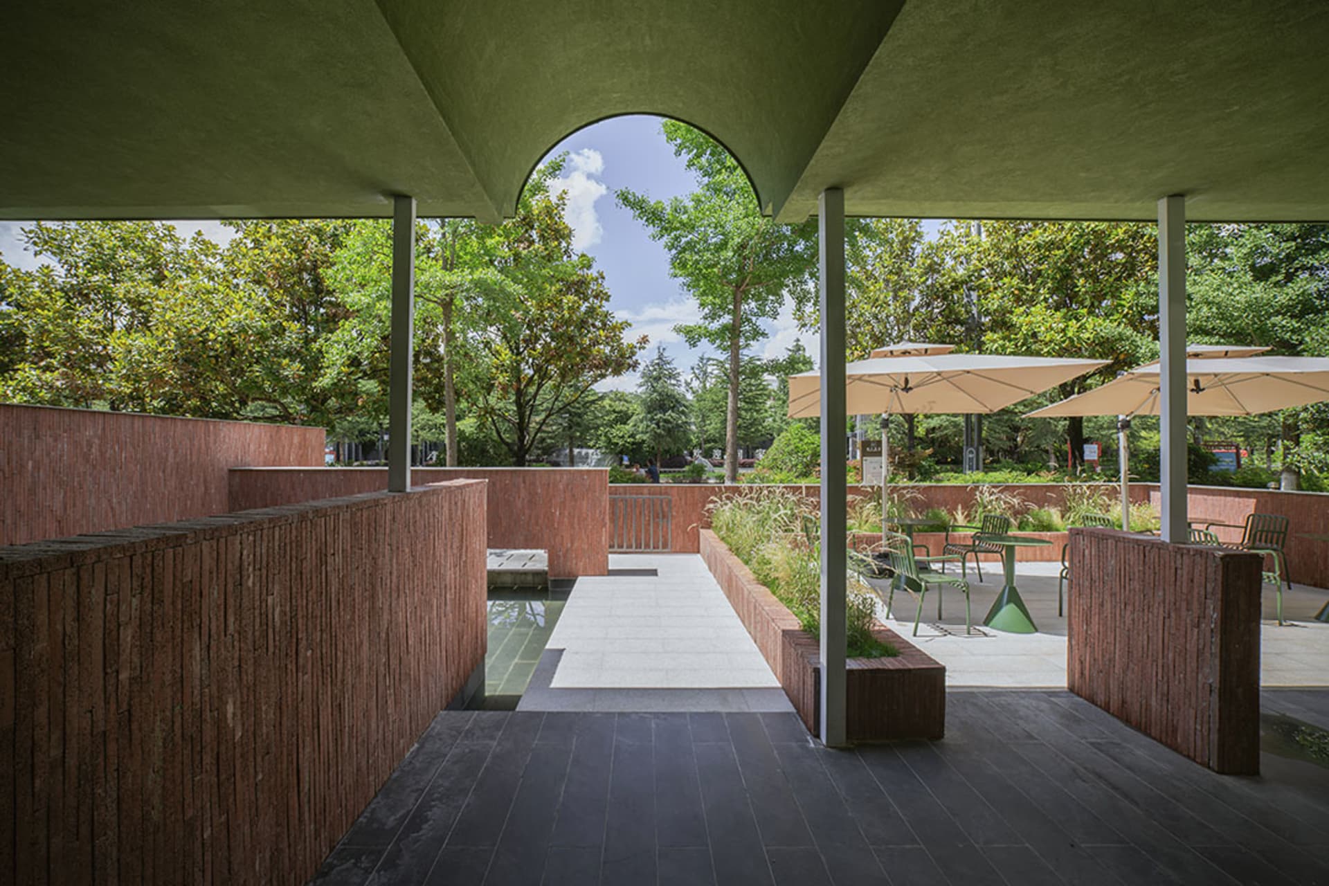 A modern outdoor patio with a green roof, surrounded by trees, featuring a dining table and chairs, with soft and warm lighting