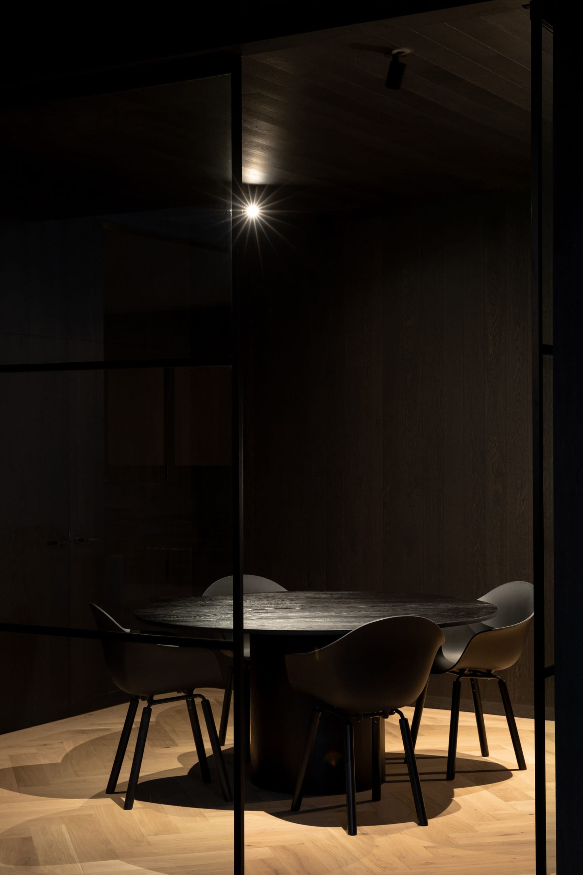 Dimly lit dining area with a black glass-topped table surrounded by wooden chairs, creating a cozy atmosphere