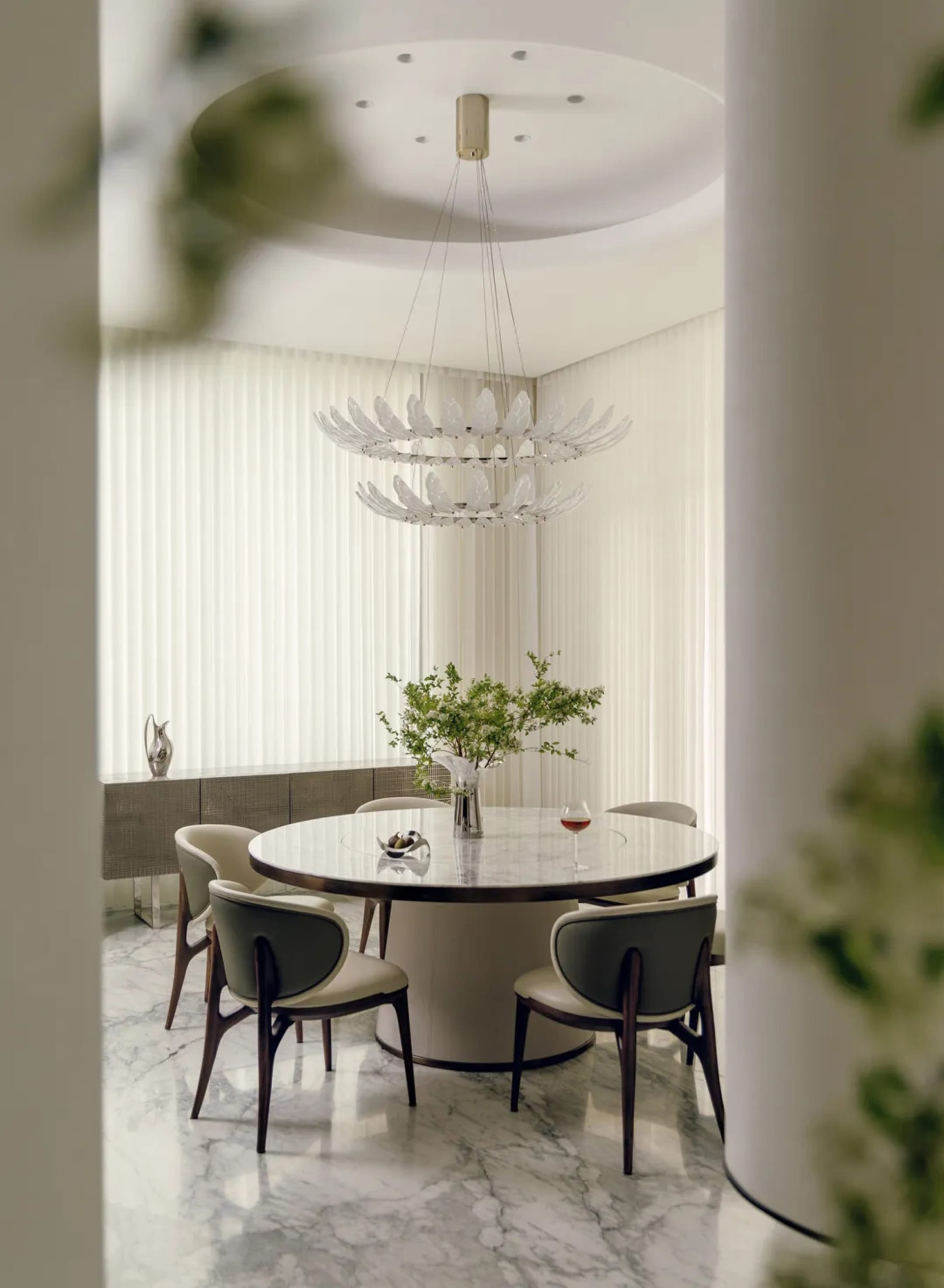 Dining room with a round table set for a meal, surrounded by chairs and a potted plant, in a well-lit and inviting space