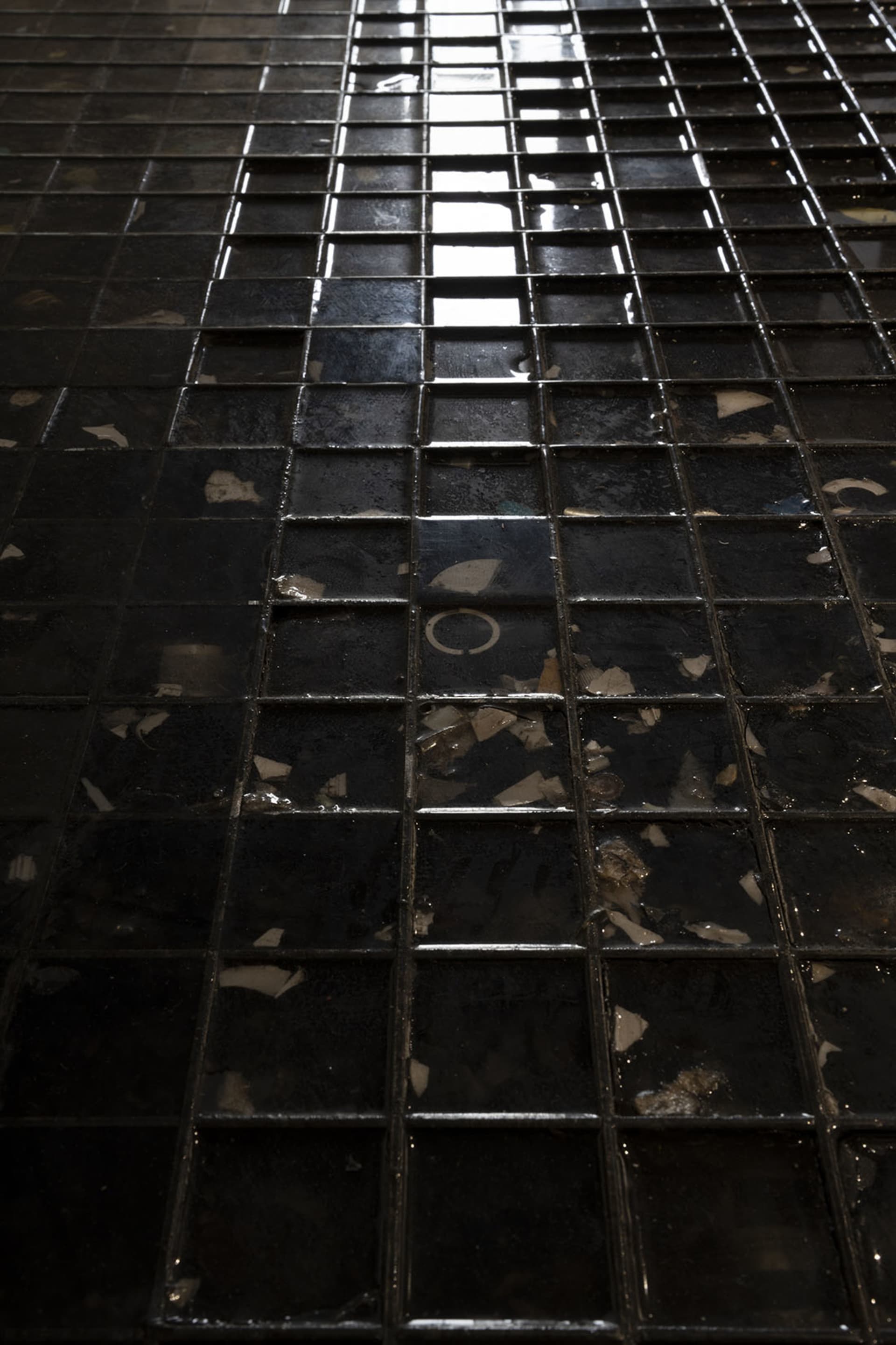 A dimly lit black and white photograph of a tile floor, possibly in a bathroom, with a minimalist and functional style
