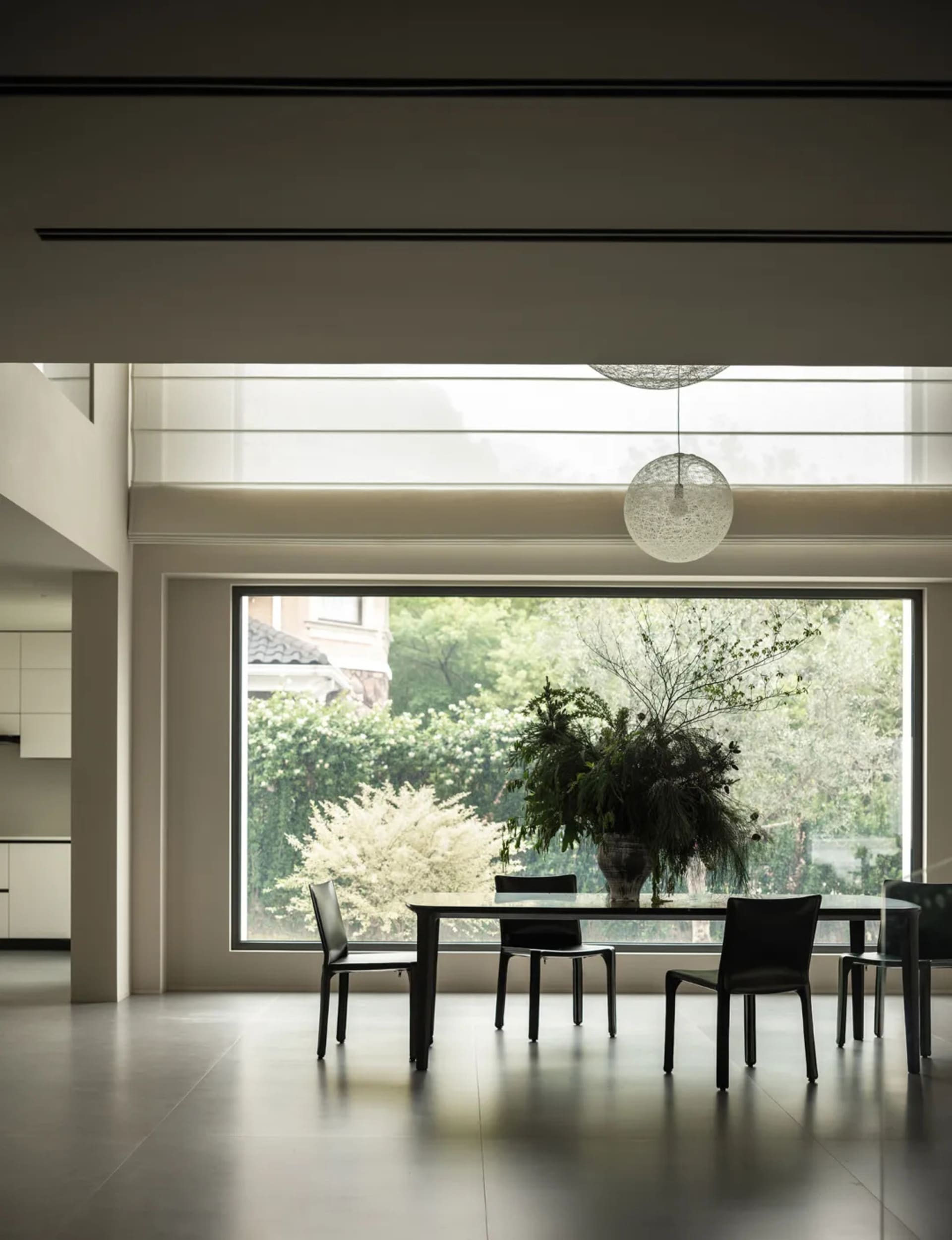 Modern living room with a dining table, chairs, and a large window allowing natural light to fill the space, surrounded by clean lines and minimalistic decor
