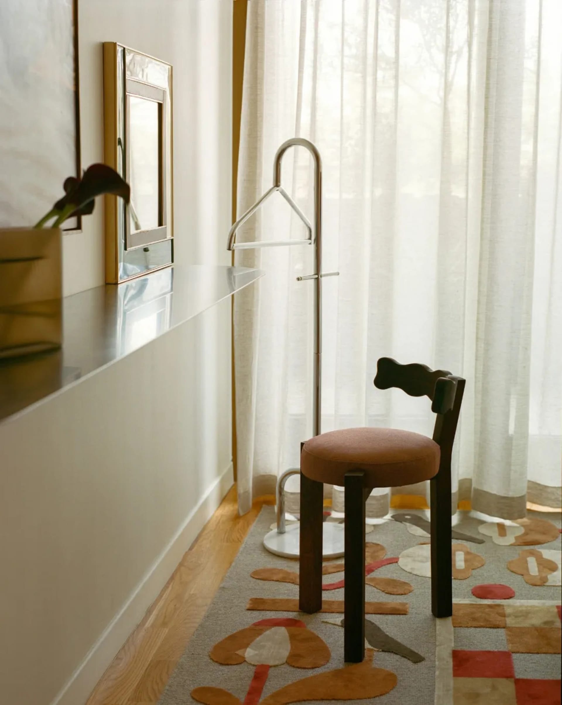 A simple bedroom with a wooden chair and mirror, surrounded by a bed and soft warm lighting