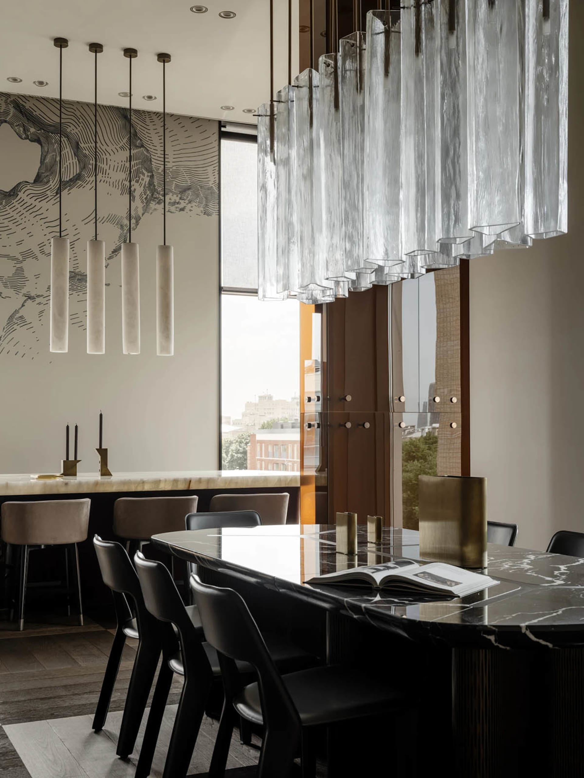 Modern kitchen with a black marble countertop, glass chandelier, dining table, and potted plants, surrounded by well-lit walls