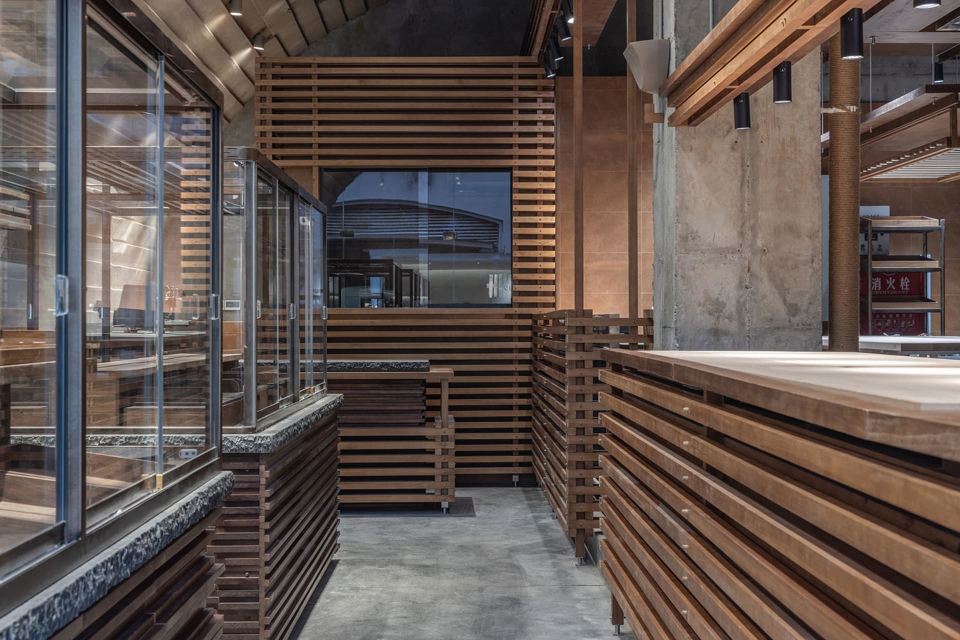 A modern restaurant interior with a wooden counter and glass front, surrounded by wooden walls, creating a warm and inviting atmosphere with dim lighting