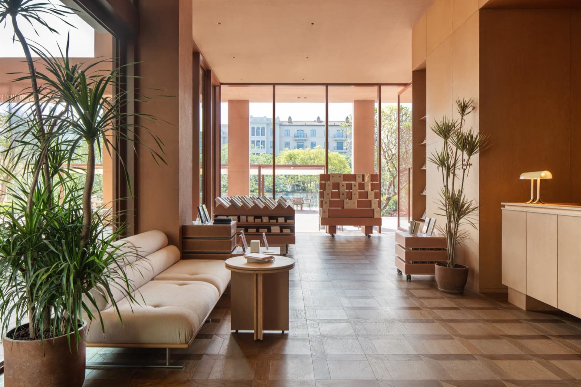 Cozy living room with a couch, coffee table, bench, books, and a potted plant near a large window