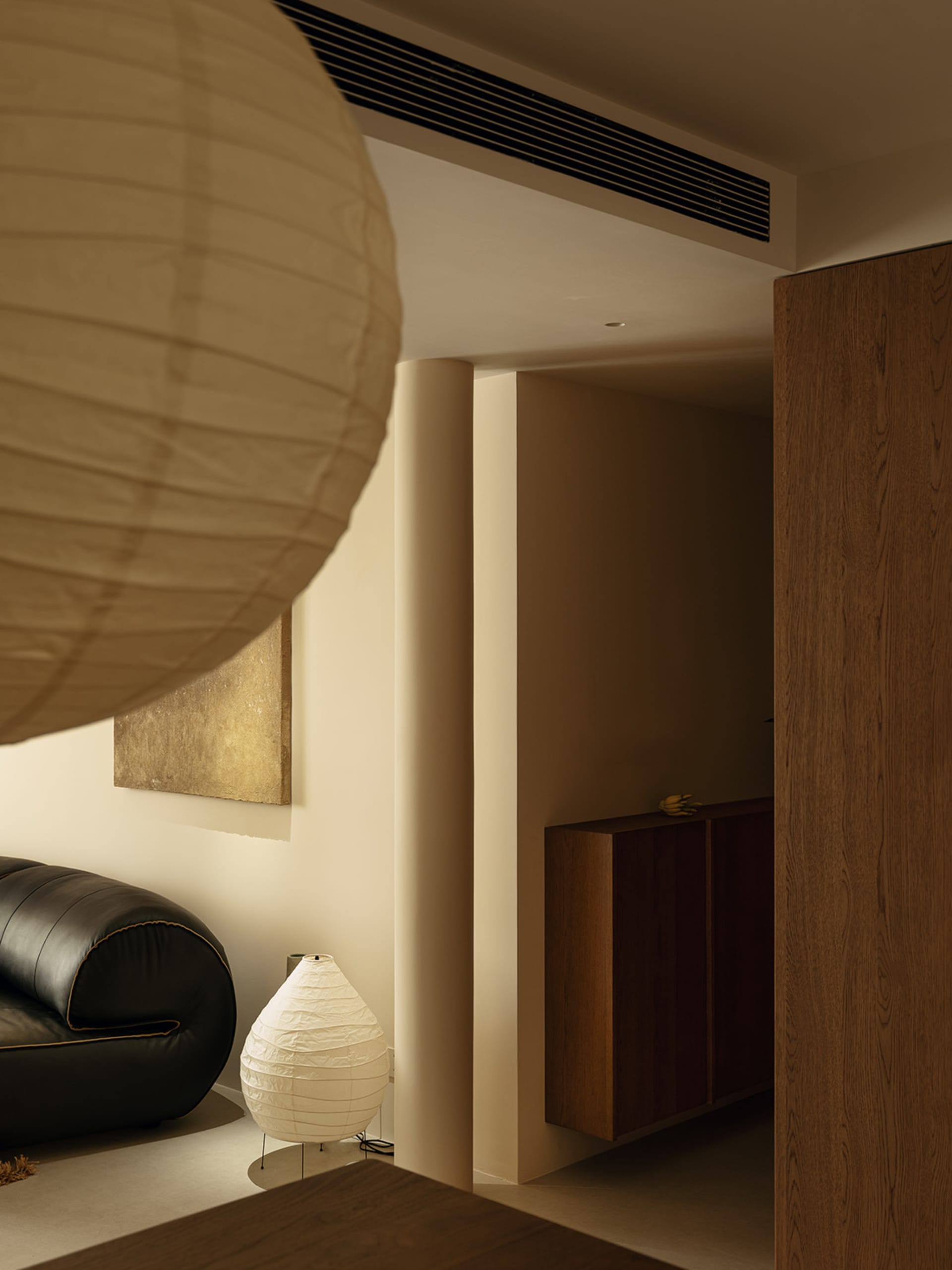 Cozy living room with a black leather sofa and a white lamp on a dimly lit background with a brown door