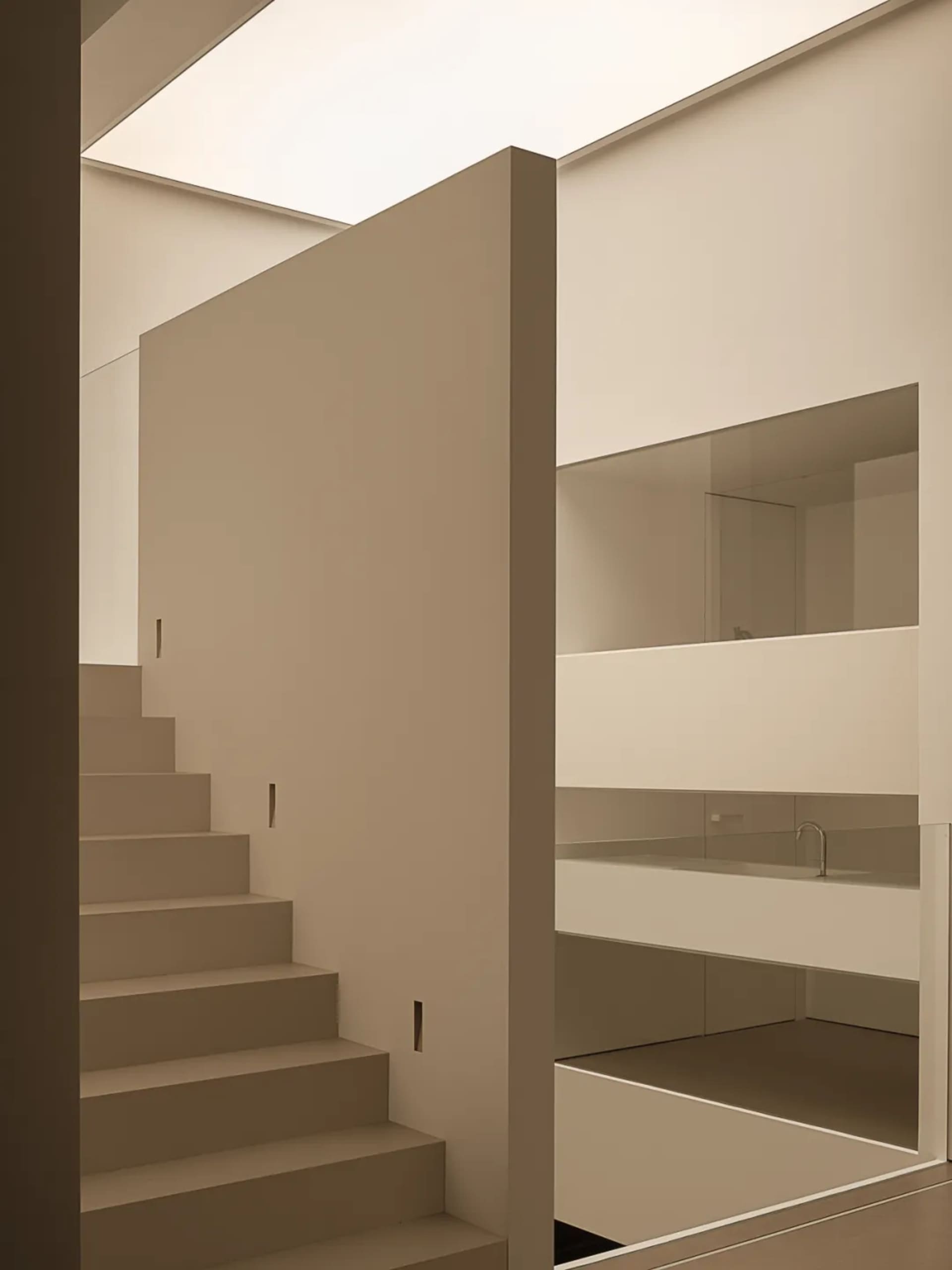 A dimly lit stairwell with concrete stairs and a glass shelf against a white wall