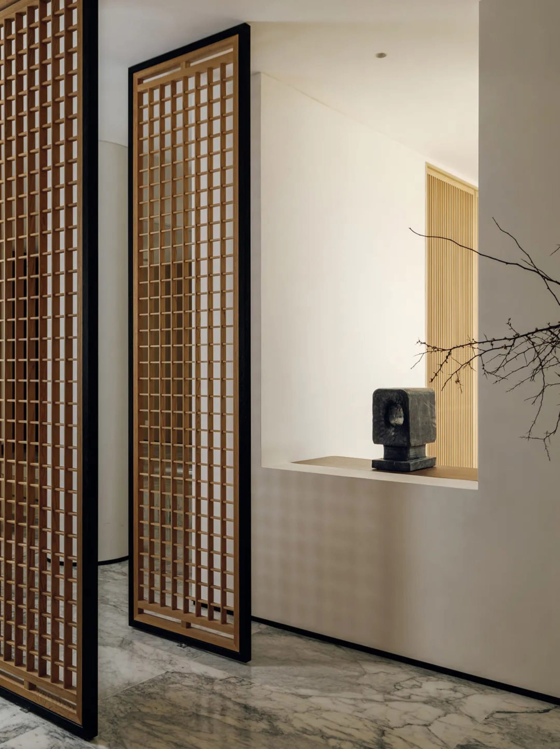 A well-lit living room with a white wall, a wooden door with decorative design, and a large window