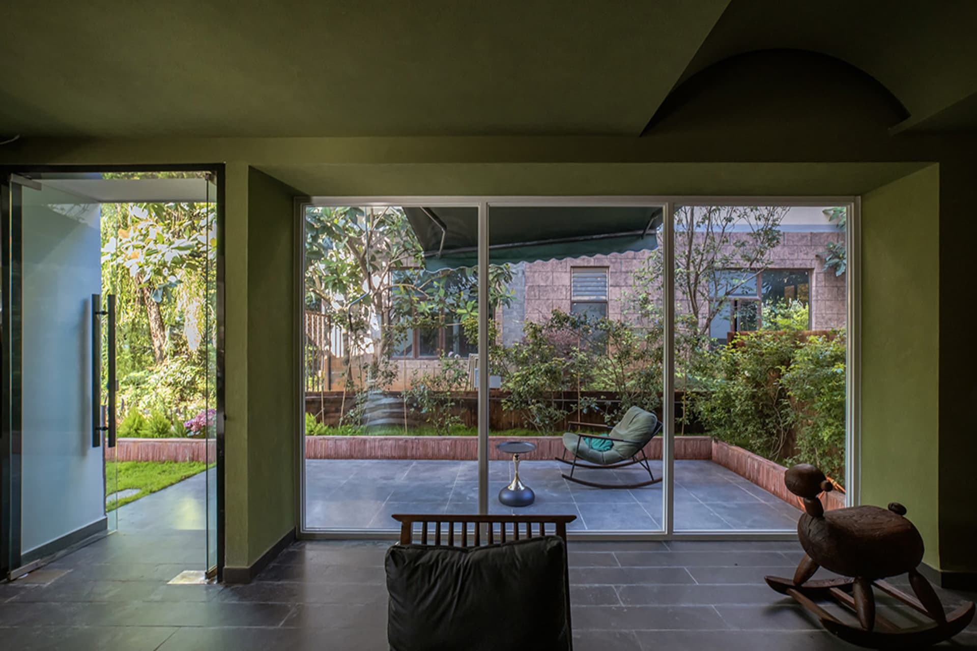 Comfortable living space with a couch, chair, and dining table, surrounded by natural light and greenery, with wood and glass materials