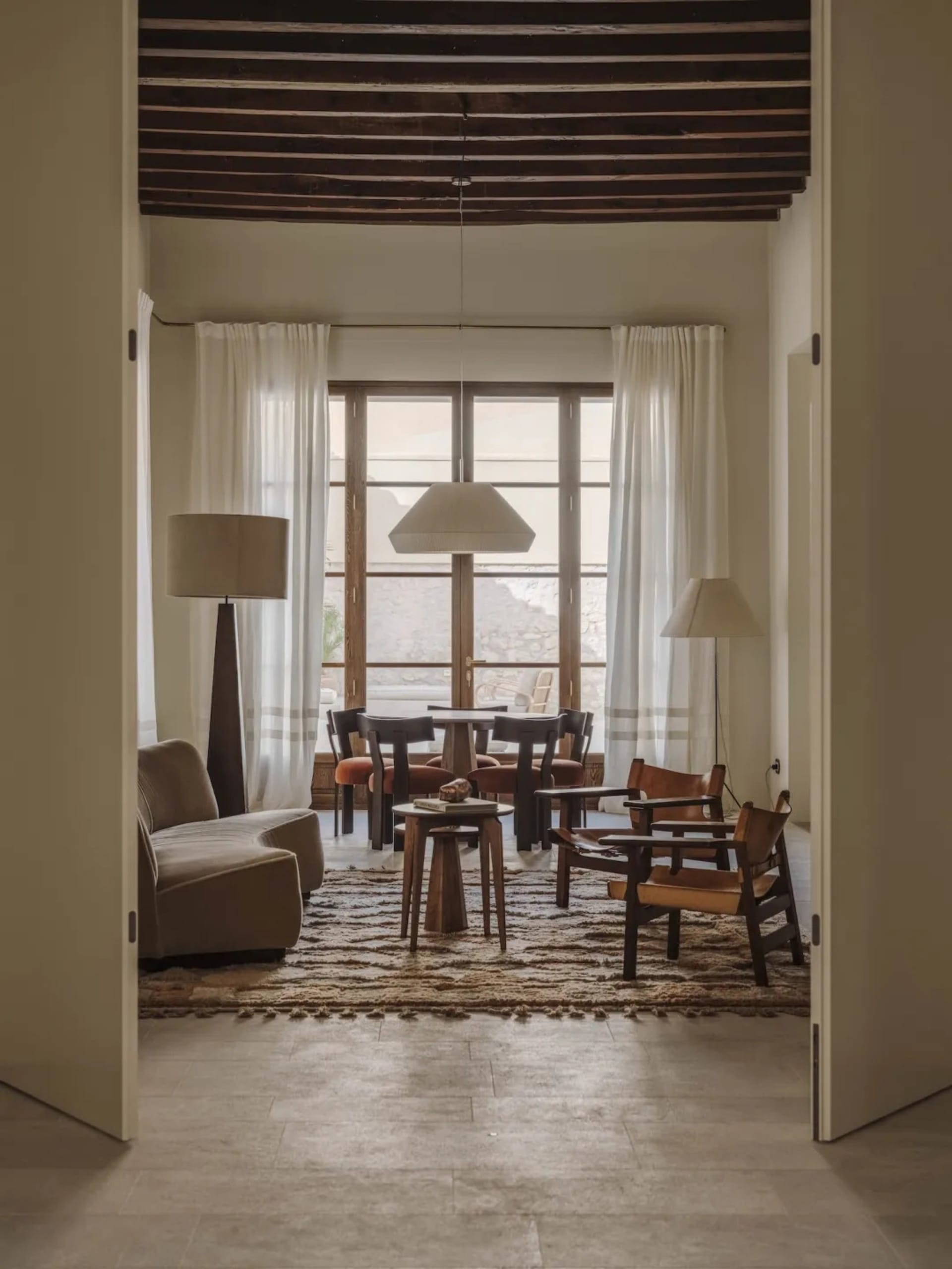 A well-lit living room with a couch, chair, dining table, and multiple chairs, decorated with a rug and lamp, creating a warm and inviting atmosphere