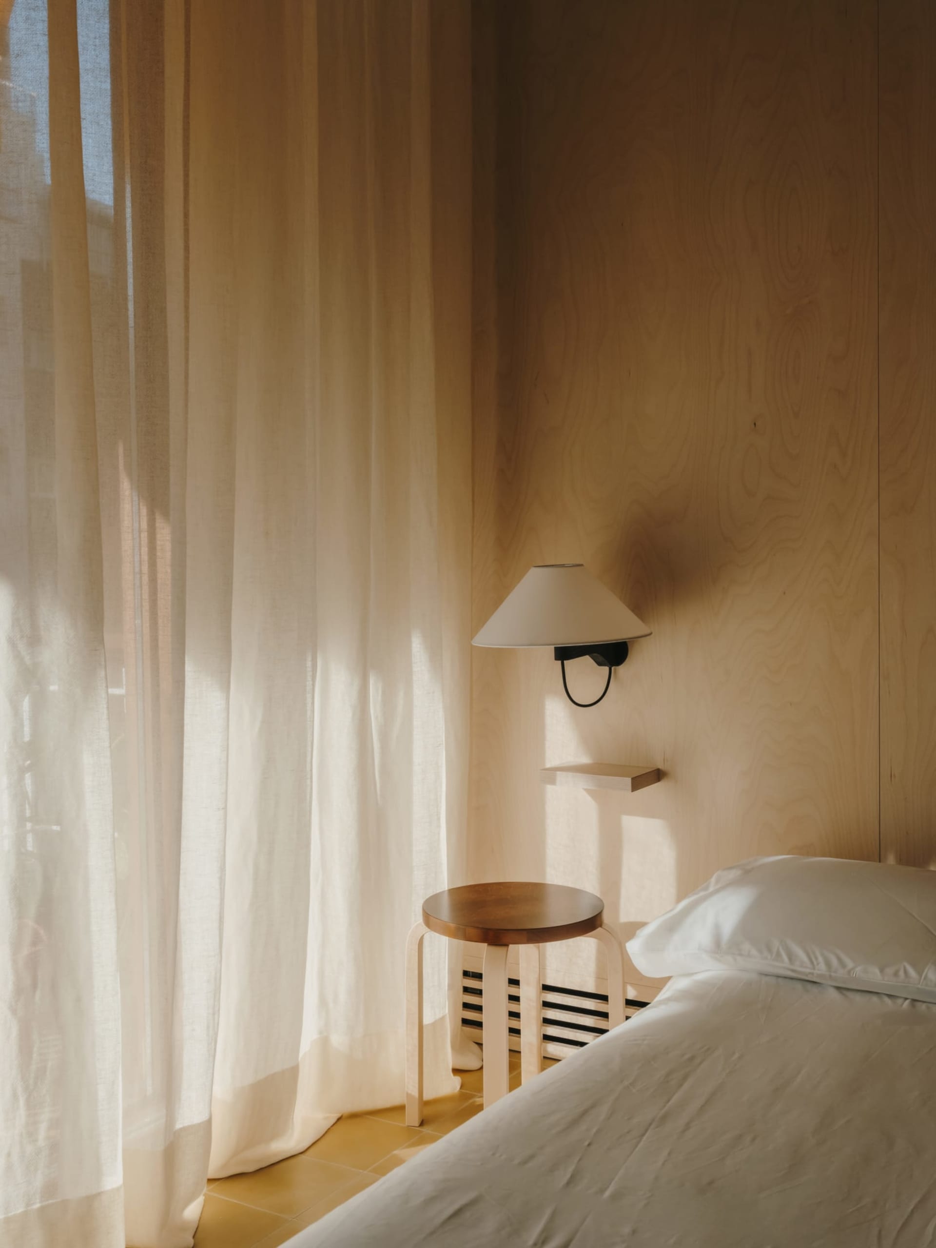 A well-lit modern bedroom with a bed, a lamp, and a chair, featuring wood and fabric materials and a calm and inviting atmosphere
