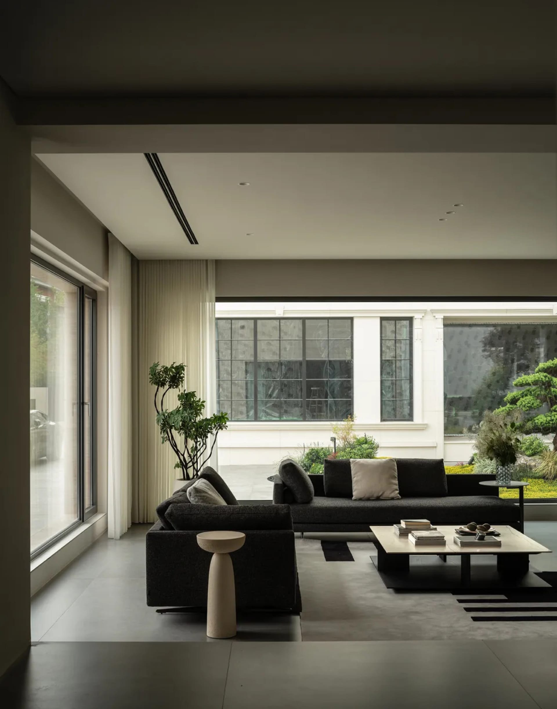 A modern living room with a black leather couch, chair, and glass coffee table, surrounded by clean lines and minimal decor, with natural light pouring in through a large window