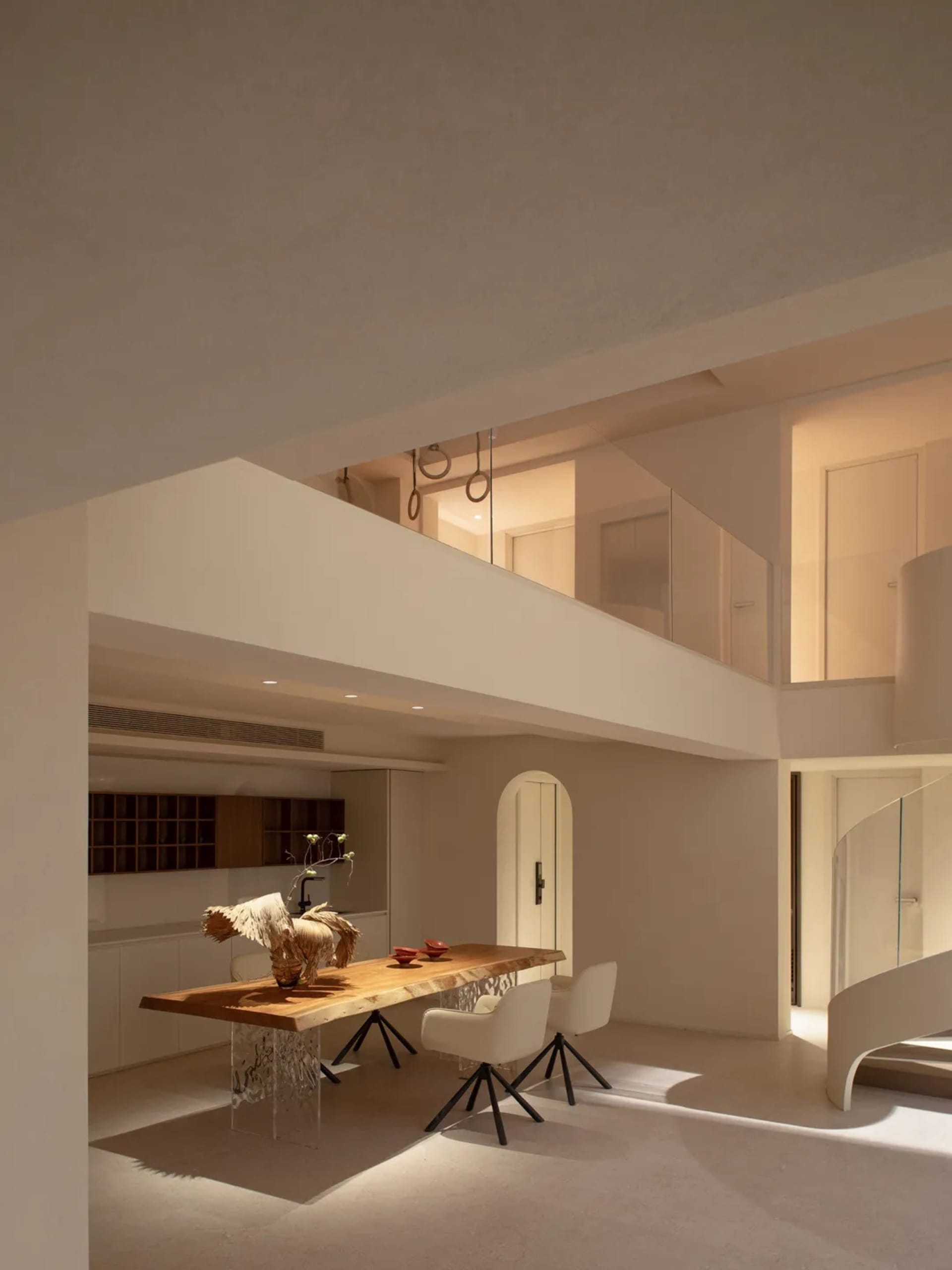 Modern kitchen with a wooden dining table, chairs, vases, and a clean minimalist design, featuring a sink and oven, with soft and diffused lighting