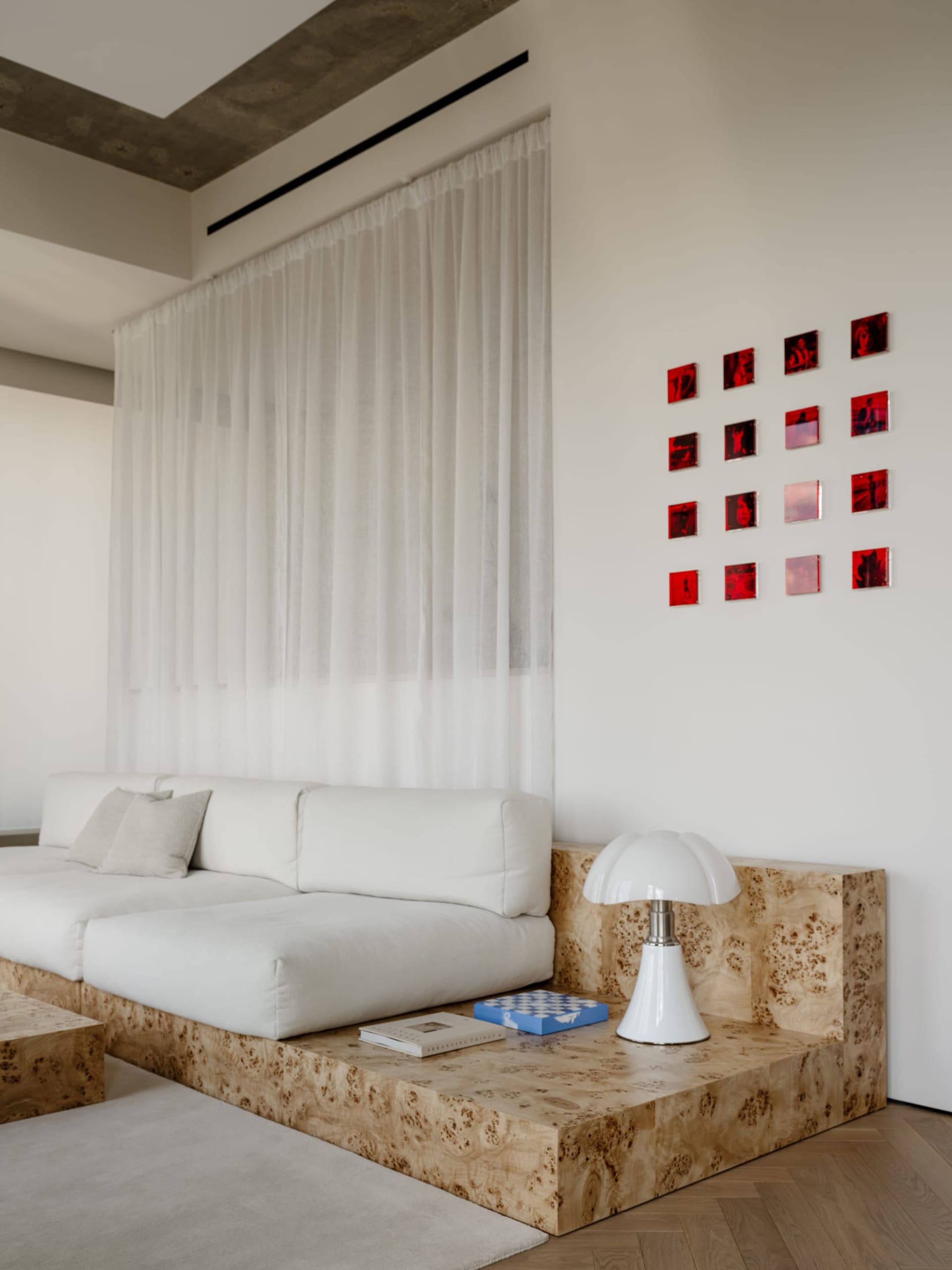 A modern living room with a white couch, chair, and lamp, surrounded by red squares on the wall, with natural light and a calm atmosphere