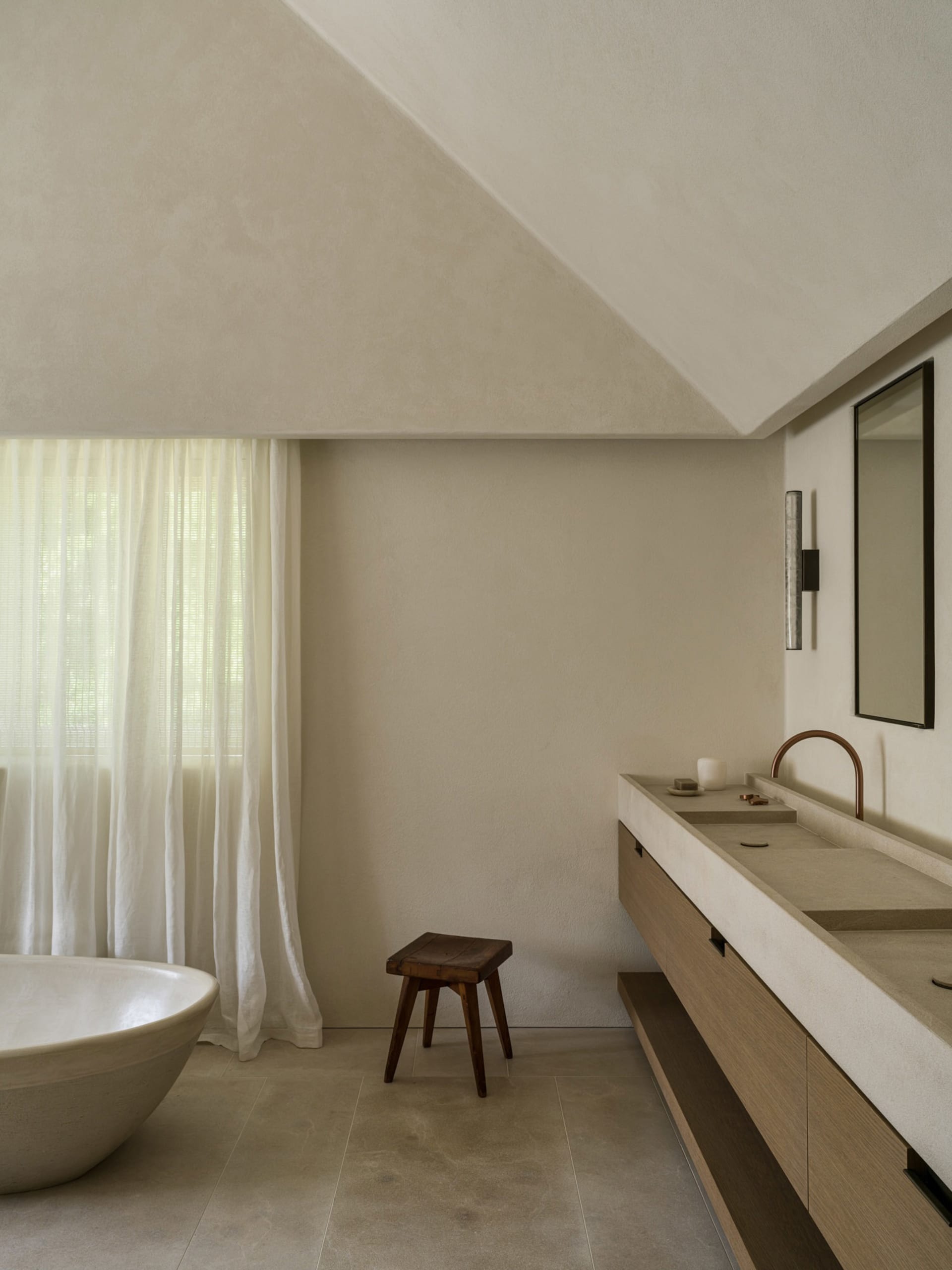 A modern bathroom with a white tub, wooden vanity, and stool, featuring a clean and minimalist design with a well-lit atmosphere