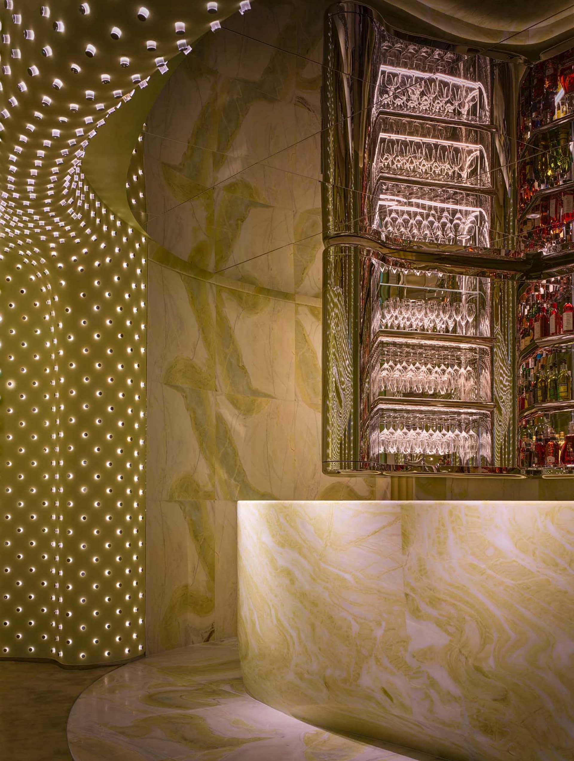 A modern bar with a marble countertop, mirrored surface, and wine glasses, surrounded by bottles and creating a sophisticated atmosphere