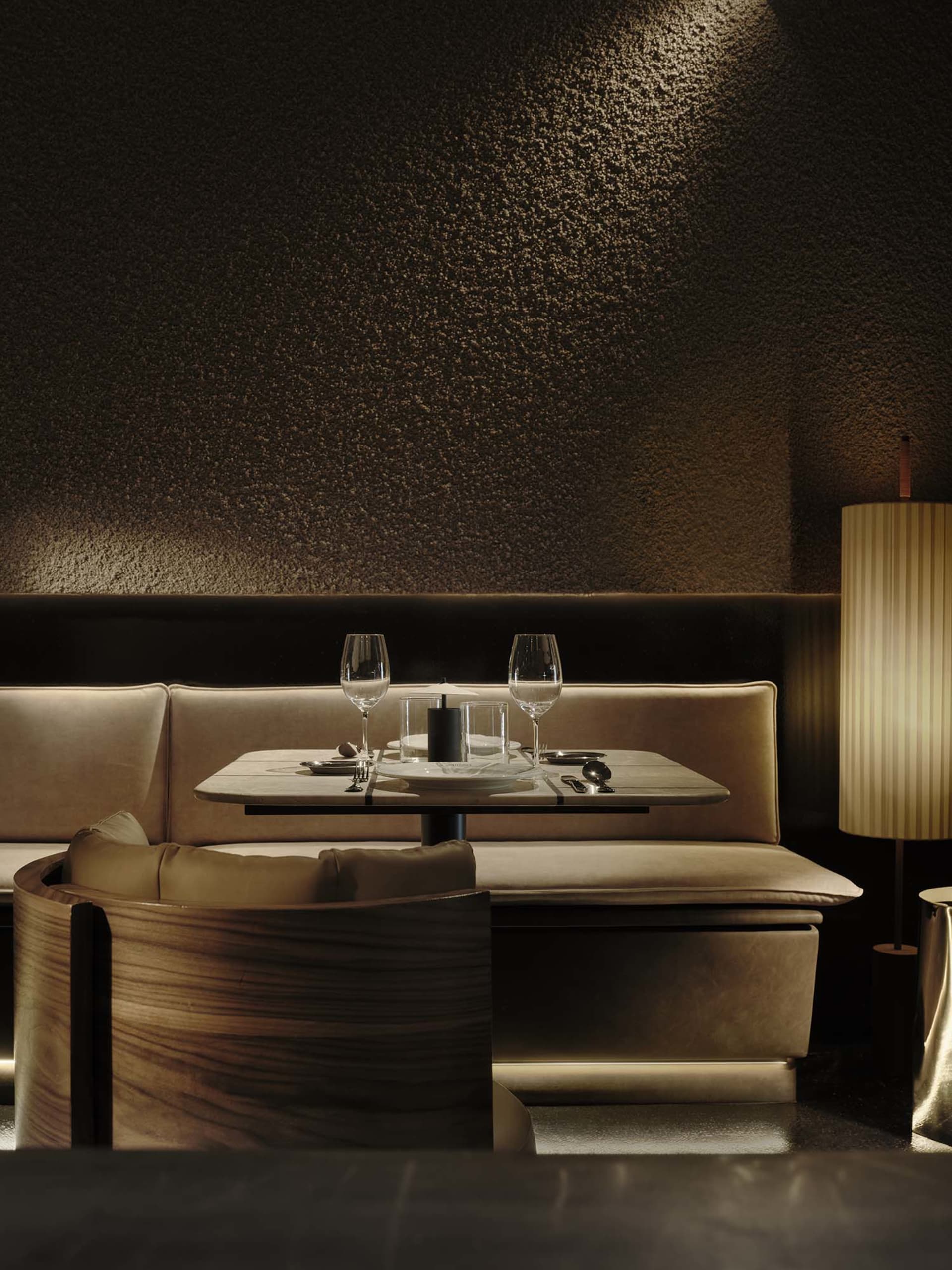 A dimly lit dining room with a wooden table, chairs, and a couch, set with wine glasses and a bottle, creating a cozy and inviting atmosphere