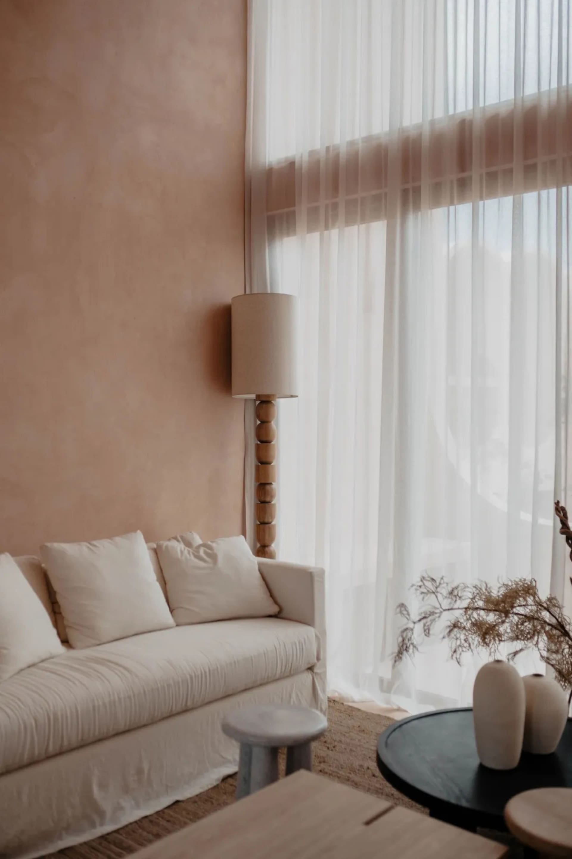 A modern living room with a white color scheme, a couch in front of a window, and a lamp nearby, creating a bright and inviting atmosphere