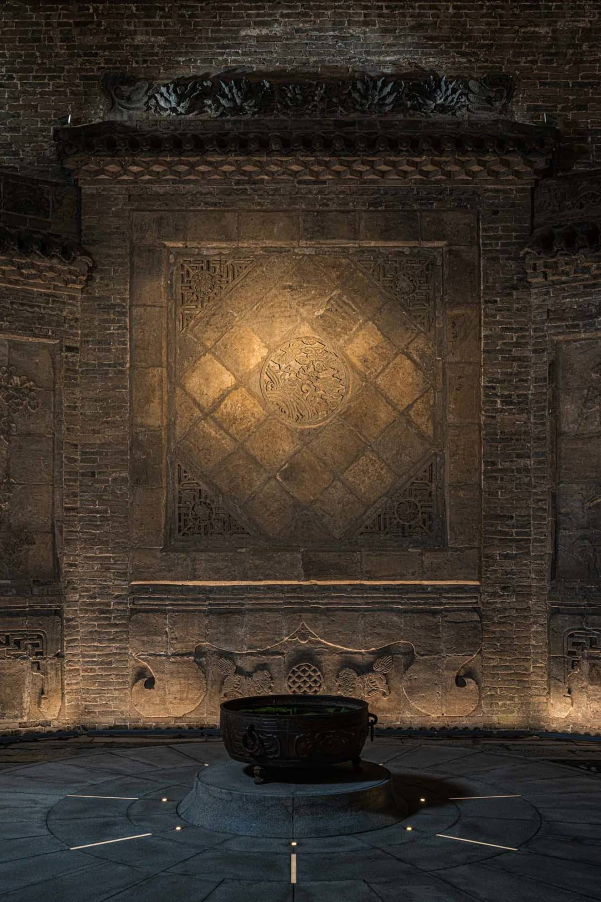 A stone wall with a stone bowl or vase on it, set in a darkened environment with dramatic shadows and textures