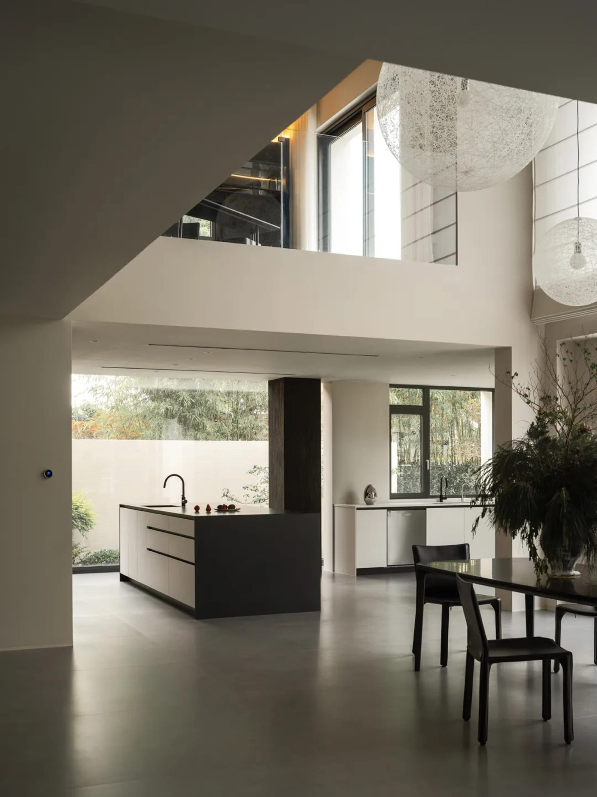 Modern kitchen with a dining area, featuring white walls, grey countertops, and wood flooring, with a potted plant and vase adding a touch of greenery and elegance