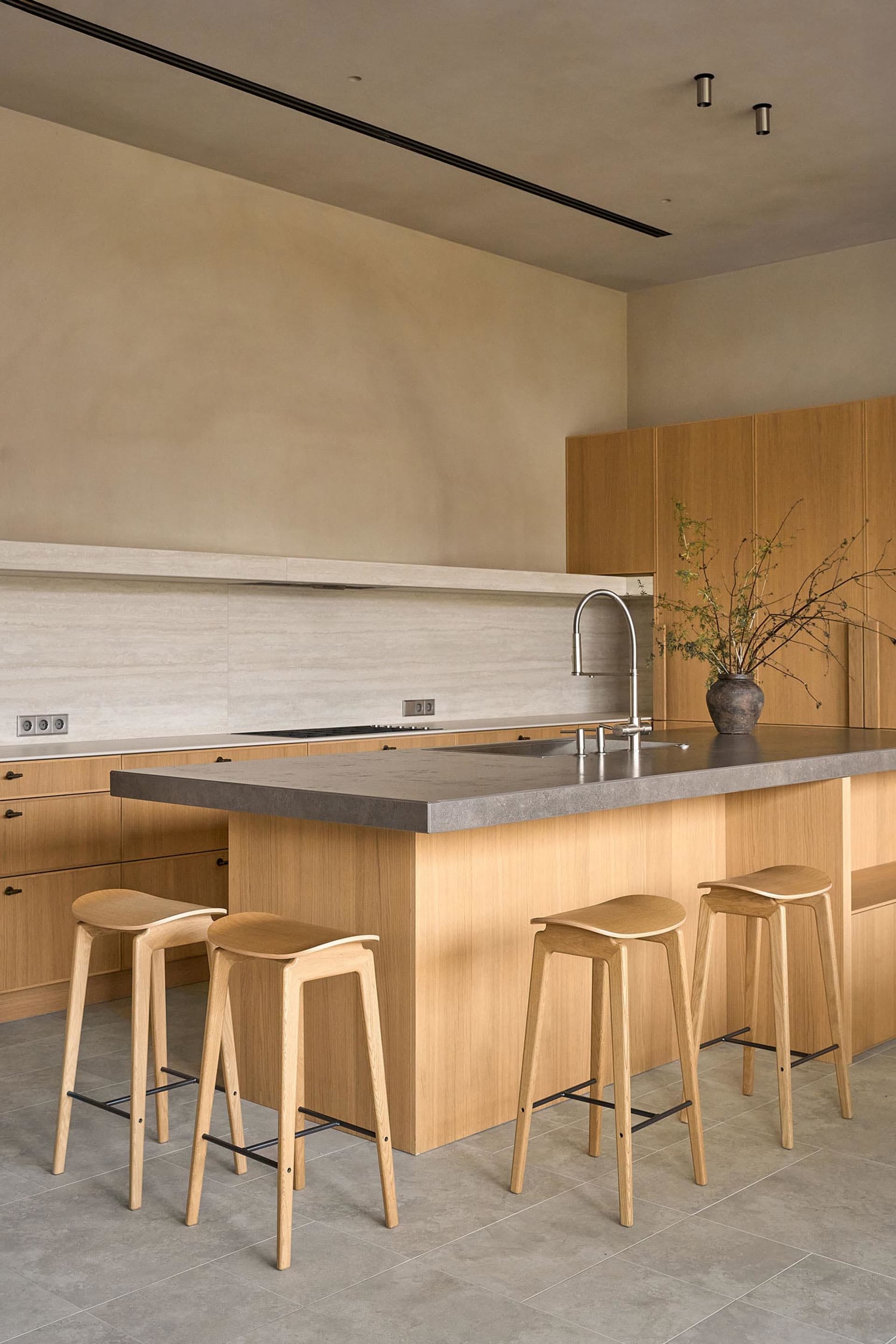 A modern kitchen with wooden cabinets, a marble countertop, and wooden stools, featuring a gray countertop and warm lighting