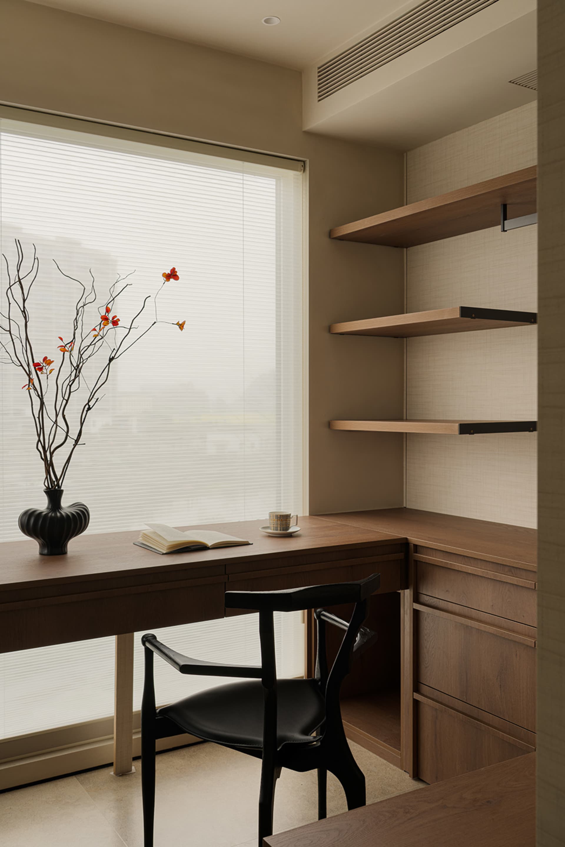 Cozy home office with a wooden desk, a black chair, and a vase with flowers on a natural light-filled room