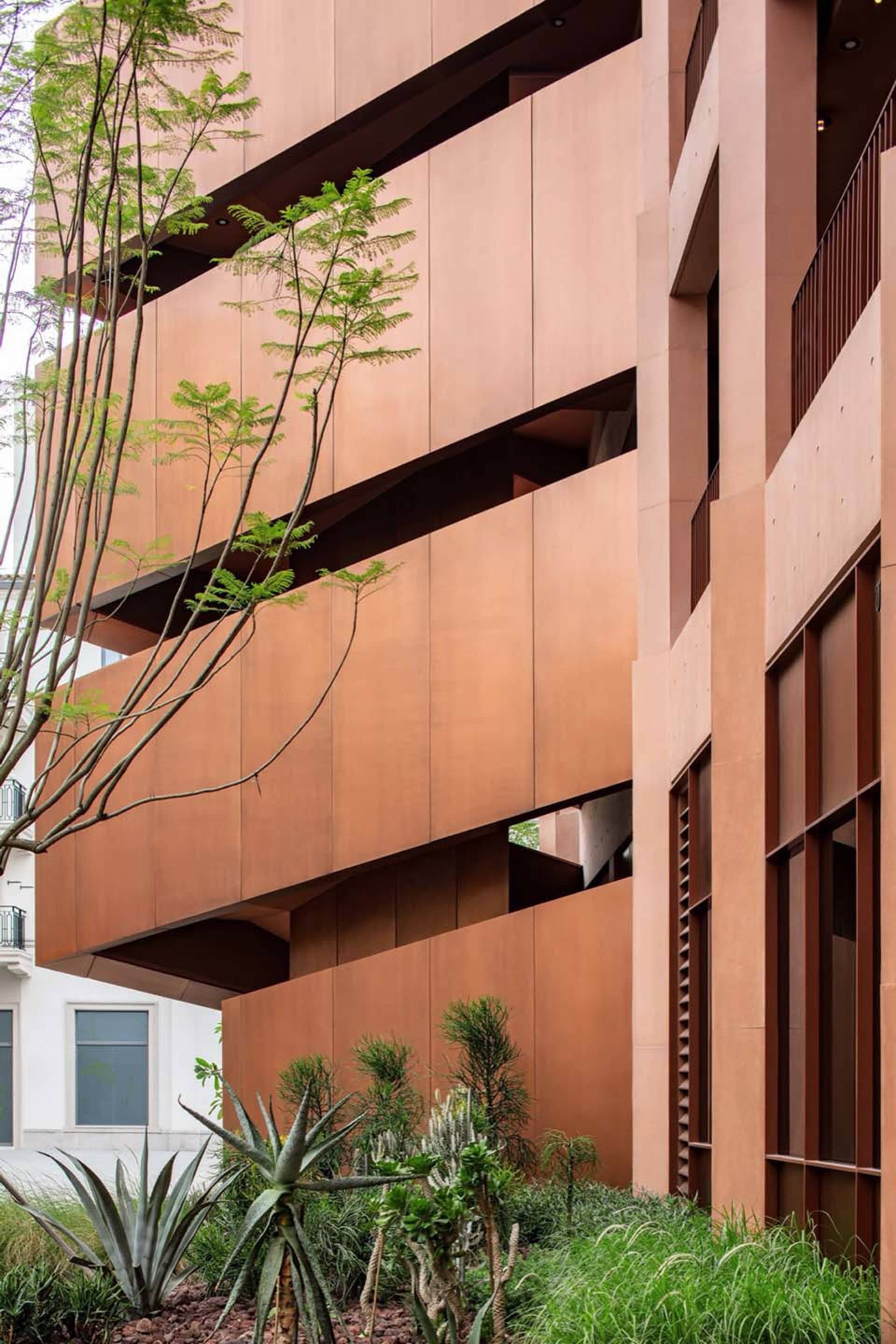 Photograph of a modern building with a brown facade, large window, and balcony, featuring a mix of wood and metal materials in a warm and inviting atmosphere
