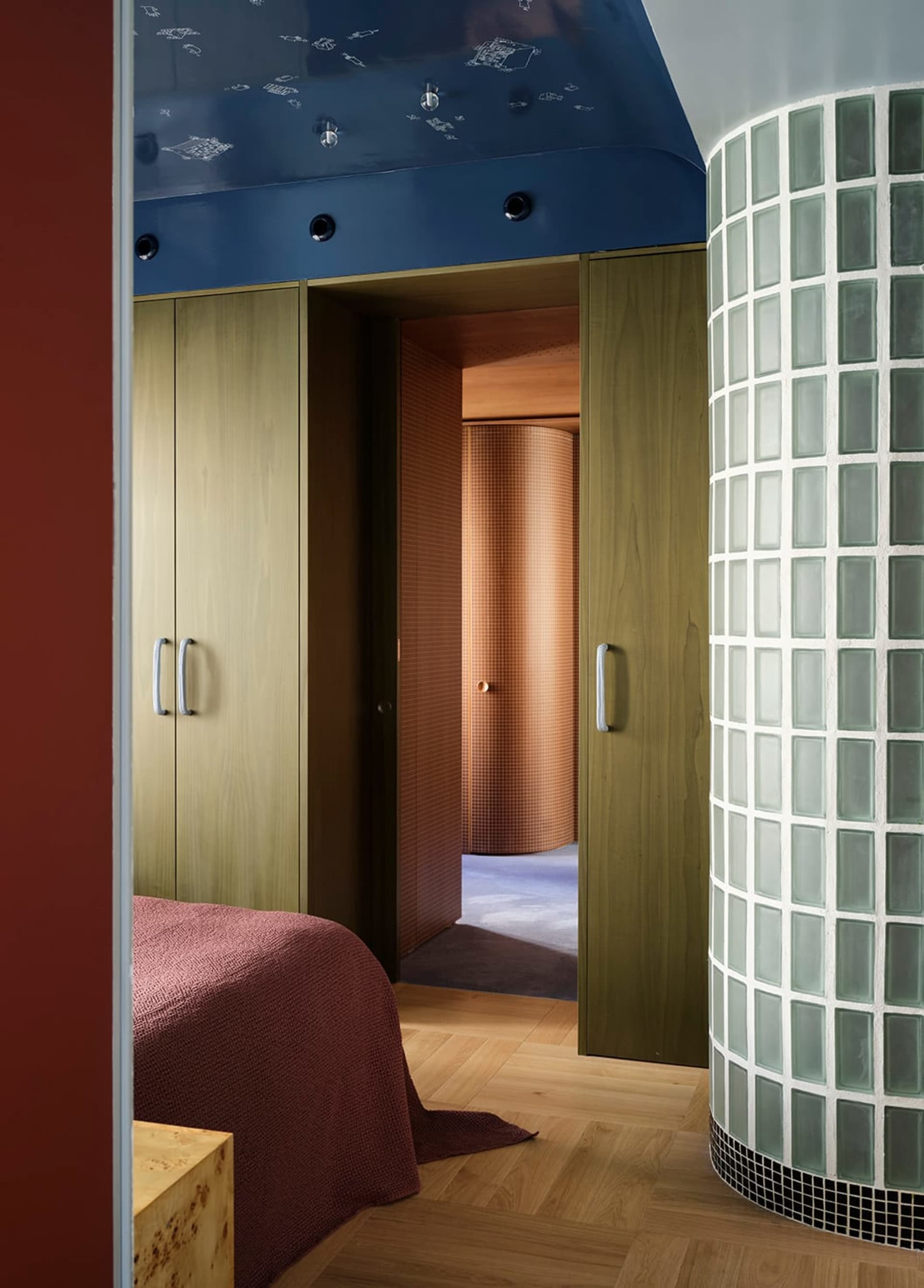 A simple bedroom with a bed, closet, and door, featuring a red accent wall and a brown door, in a dimly lit space
