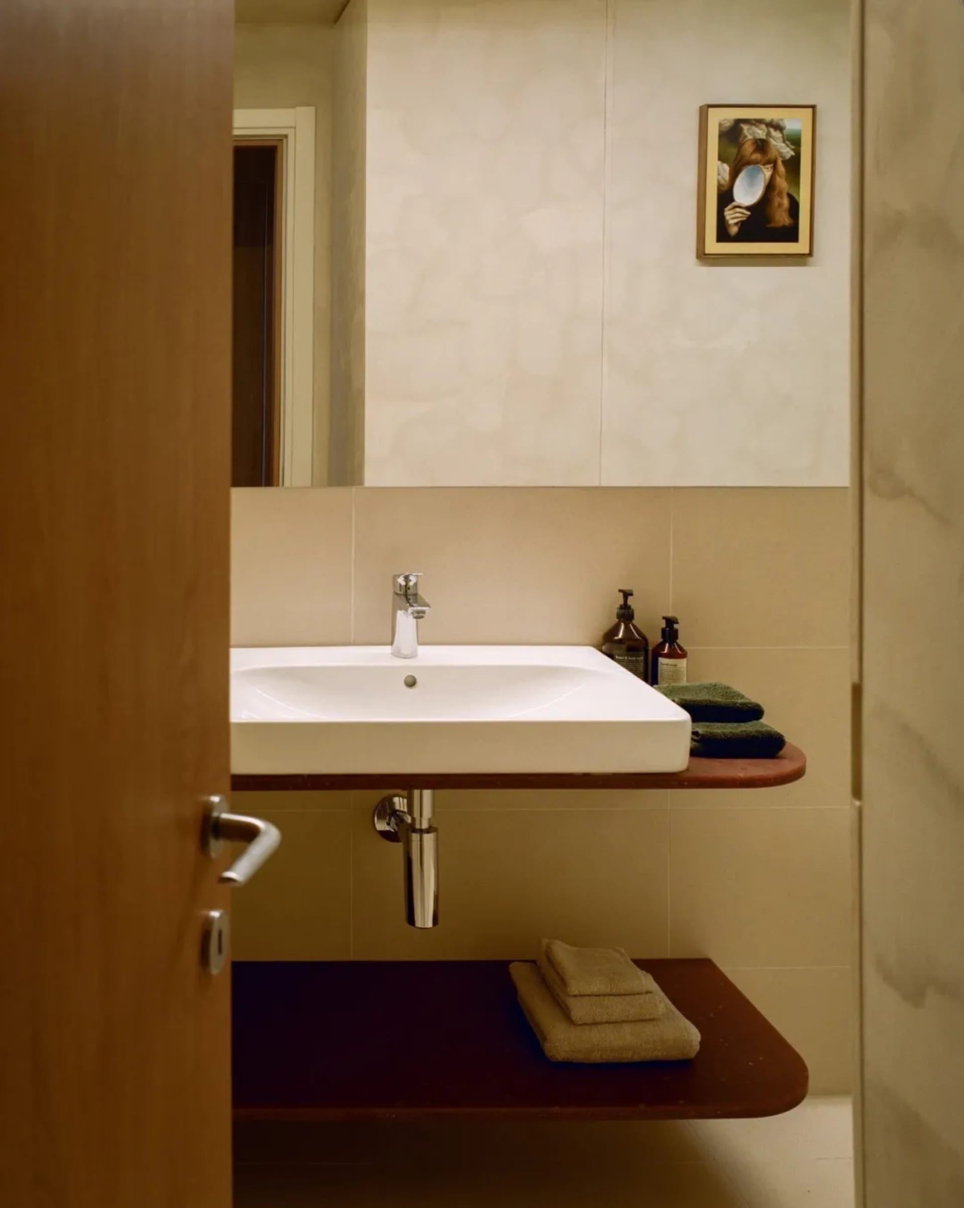 Modern bathroom with a white sink, brown tile floor, and a towel rack on the right side, under dim lighting
