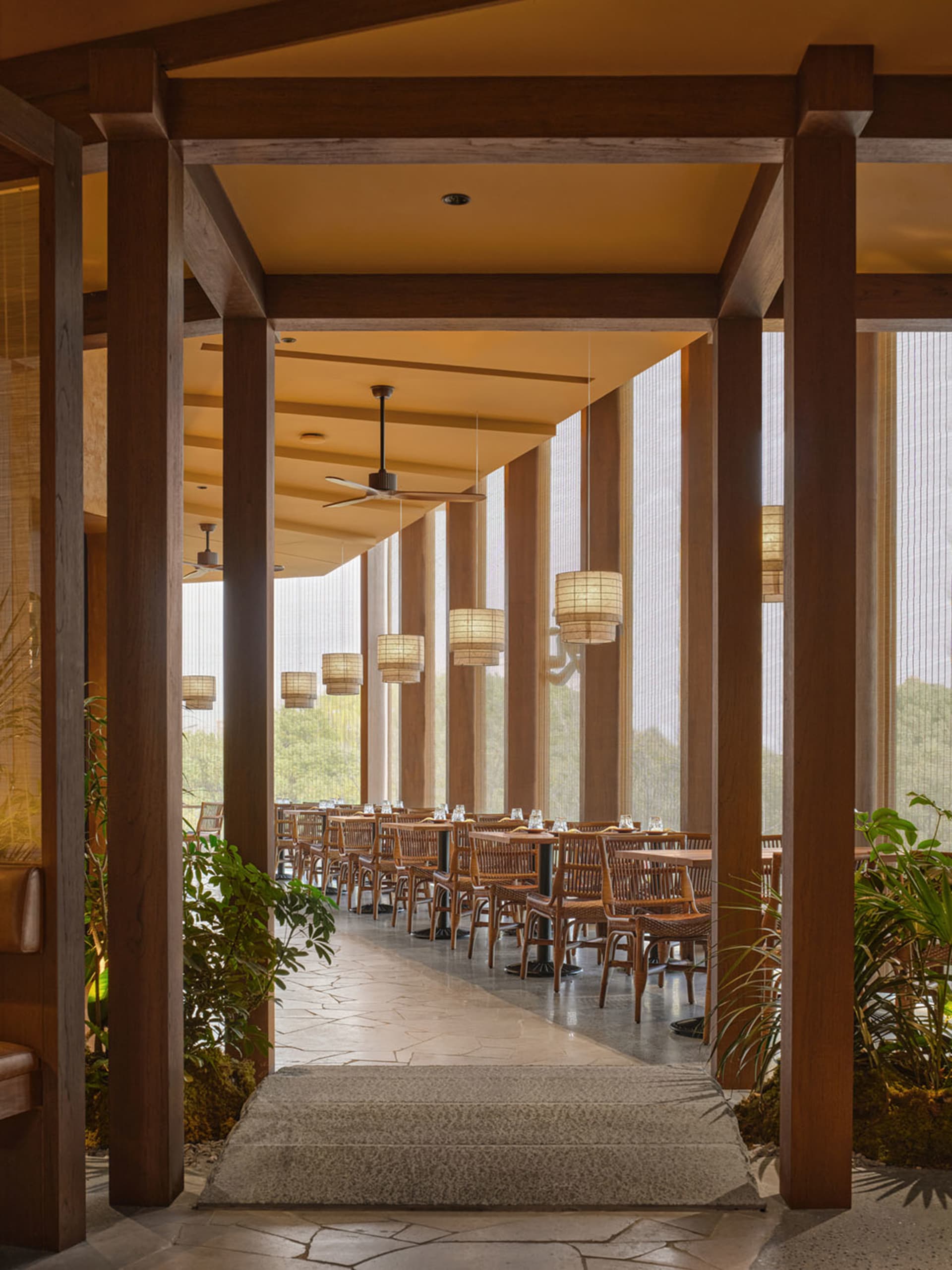Warm and inviting restaurant interior with wooden furniture, multiple dining tables, and hanging lights