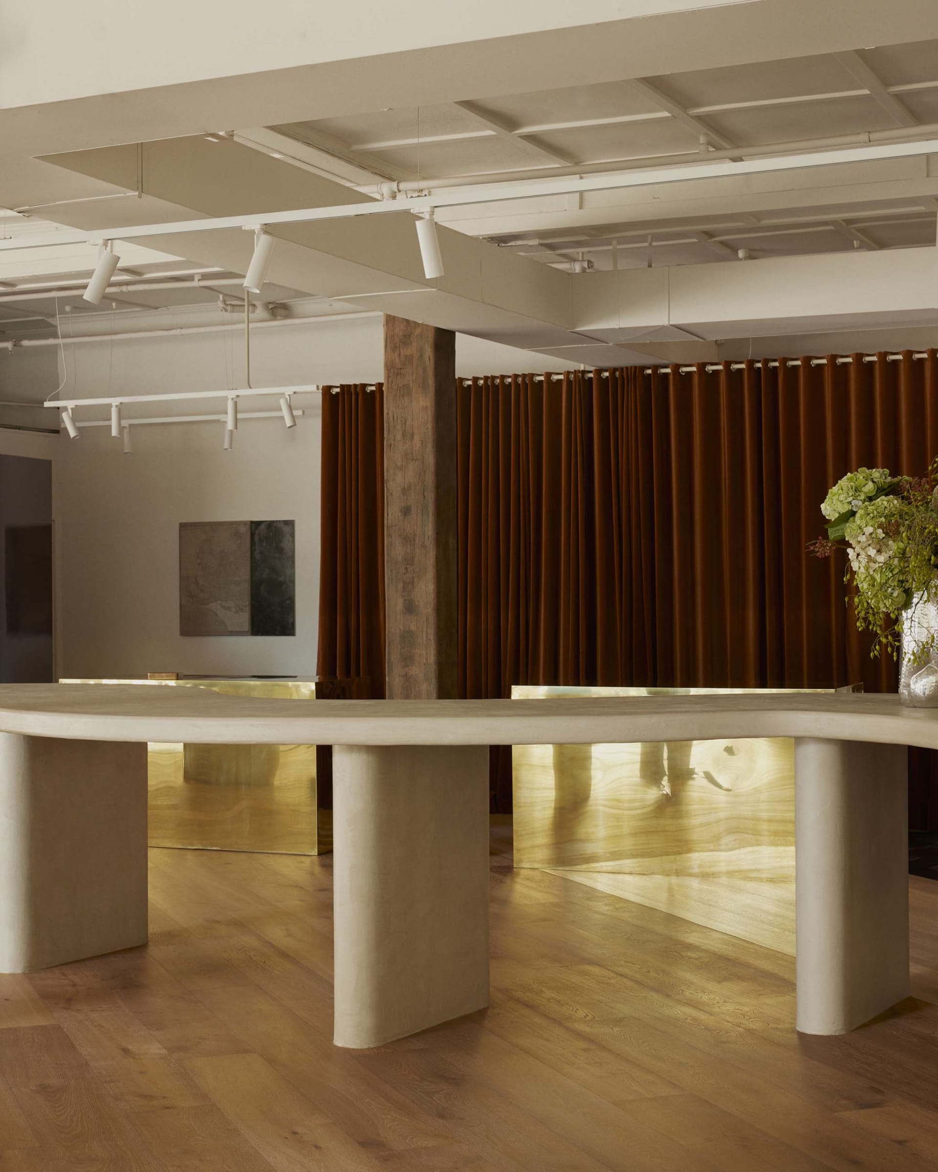 A warm and inviting dining space with a wooden floor, a long white table, and a potted plant, lit by a combination of natural and artificial light