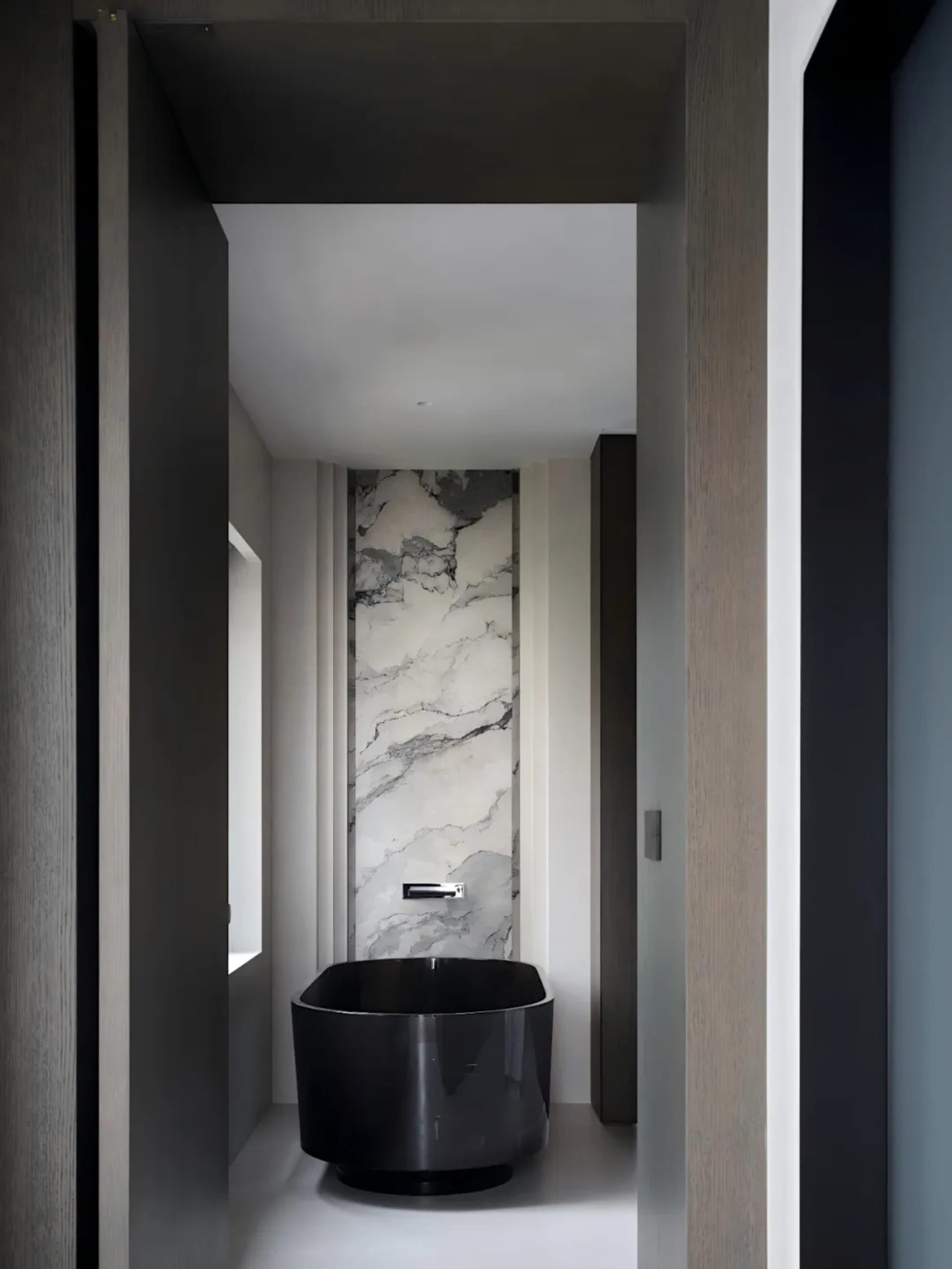 Black and white photograph of a modern bathroom with a black bathtub, toilet, and sink, set against a backdrop of marble walls in a dimly lit space