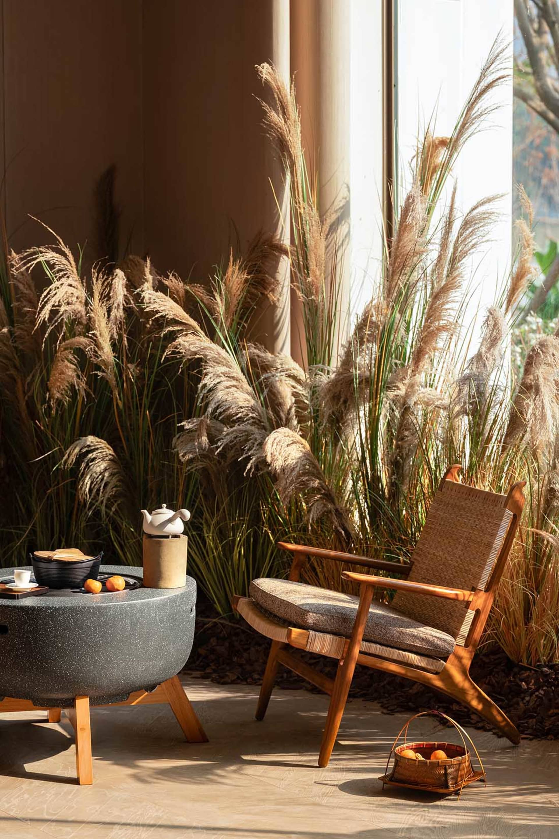A modern living room with a wooden chair, table, couch, and dining table, surrounded by potted plants and natural materials
