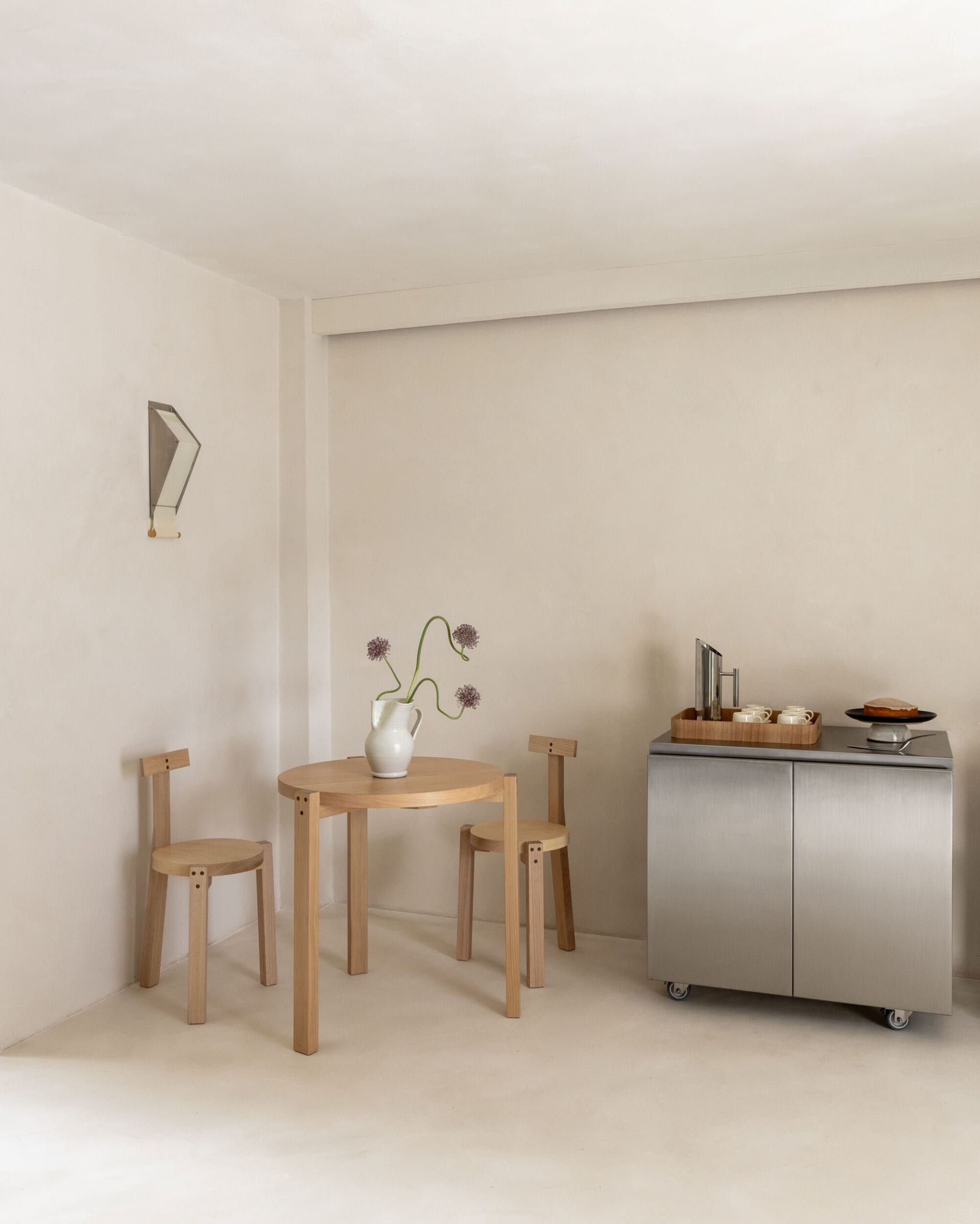 A modern kitchen with a dining table and chairs, surrounded by white cabinets, a sink, and a refrigerator, with natural light from the windows