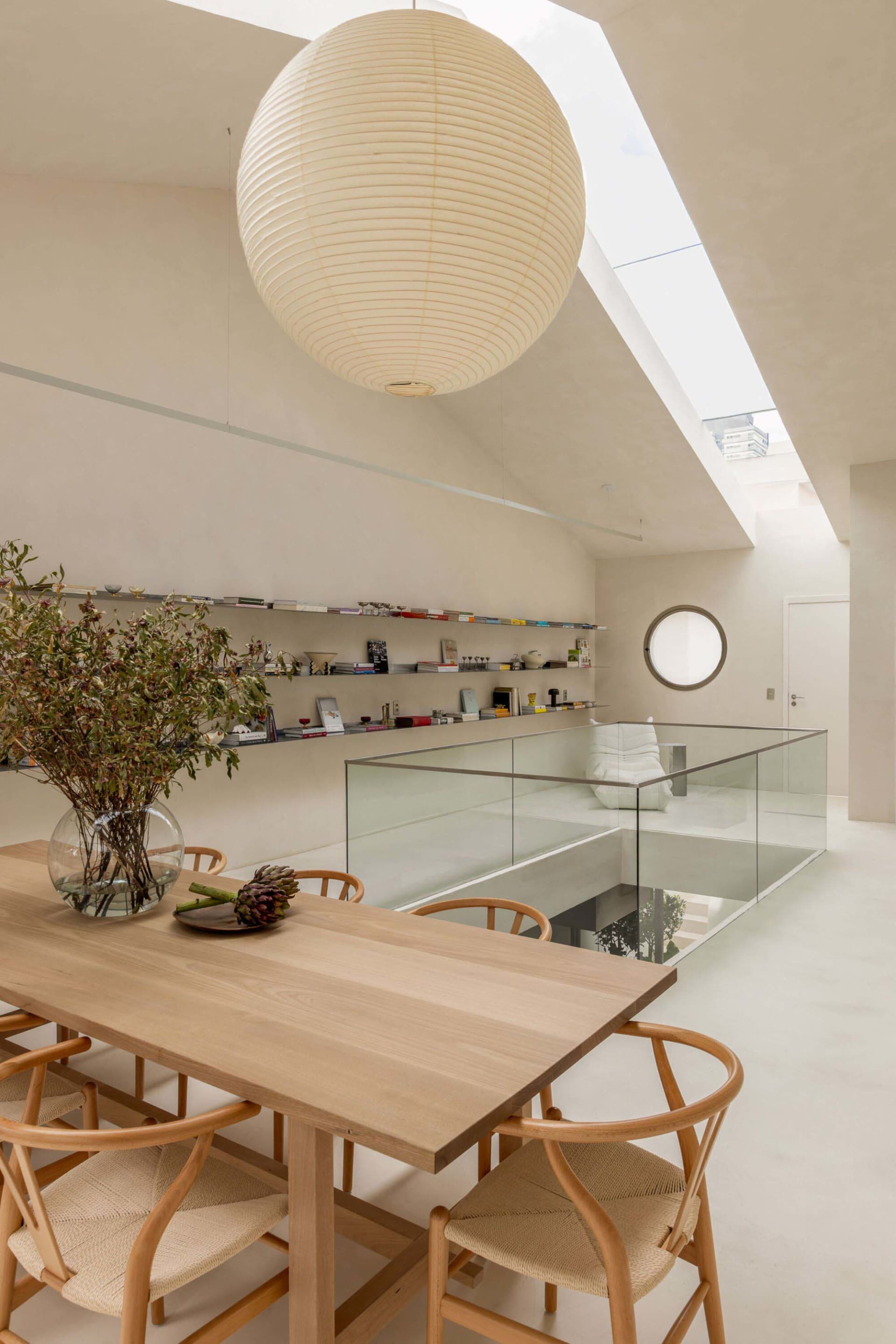 A modern living room with a glass wall, wooden dining table, and cozy atmosphere, decorated with books and potted plants