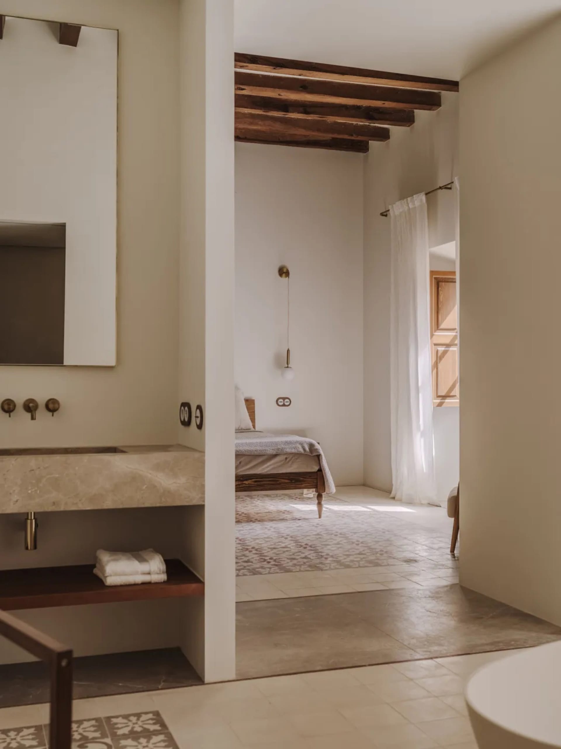 A minimalist bedroom with a bed, a wooden chair, and a white rug, well-lit by natural light from the window