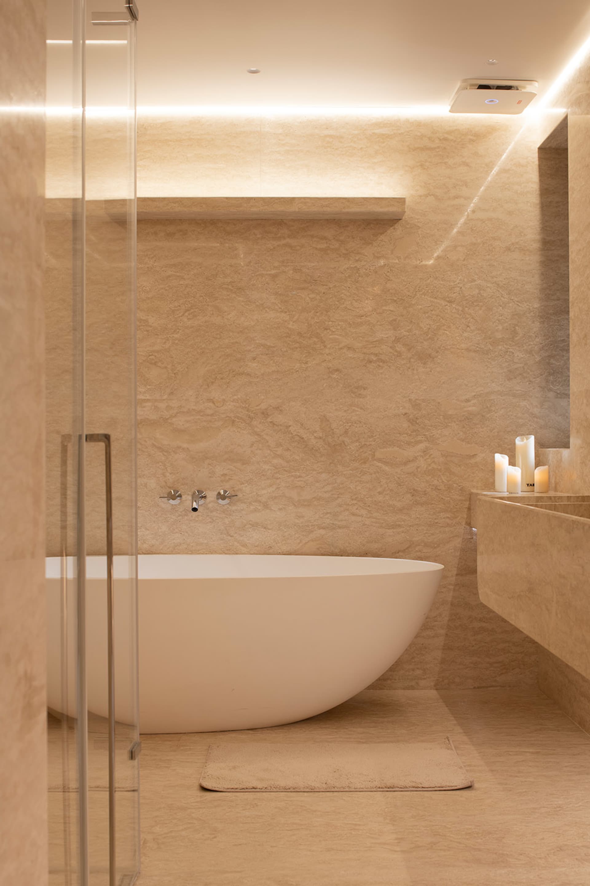 A modern bathroom with a large white bathtub, marble walls, and dim lighting
