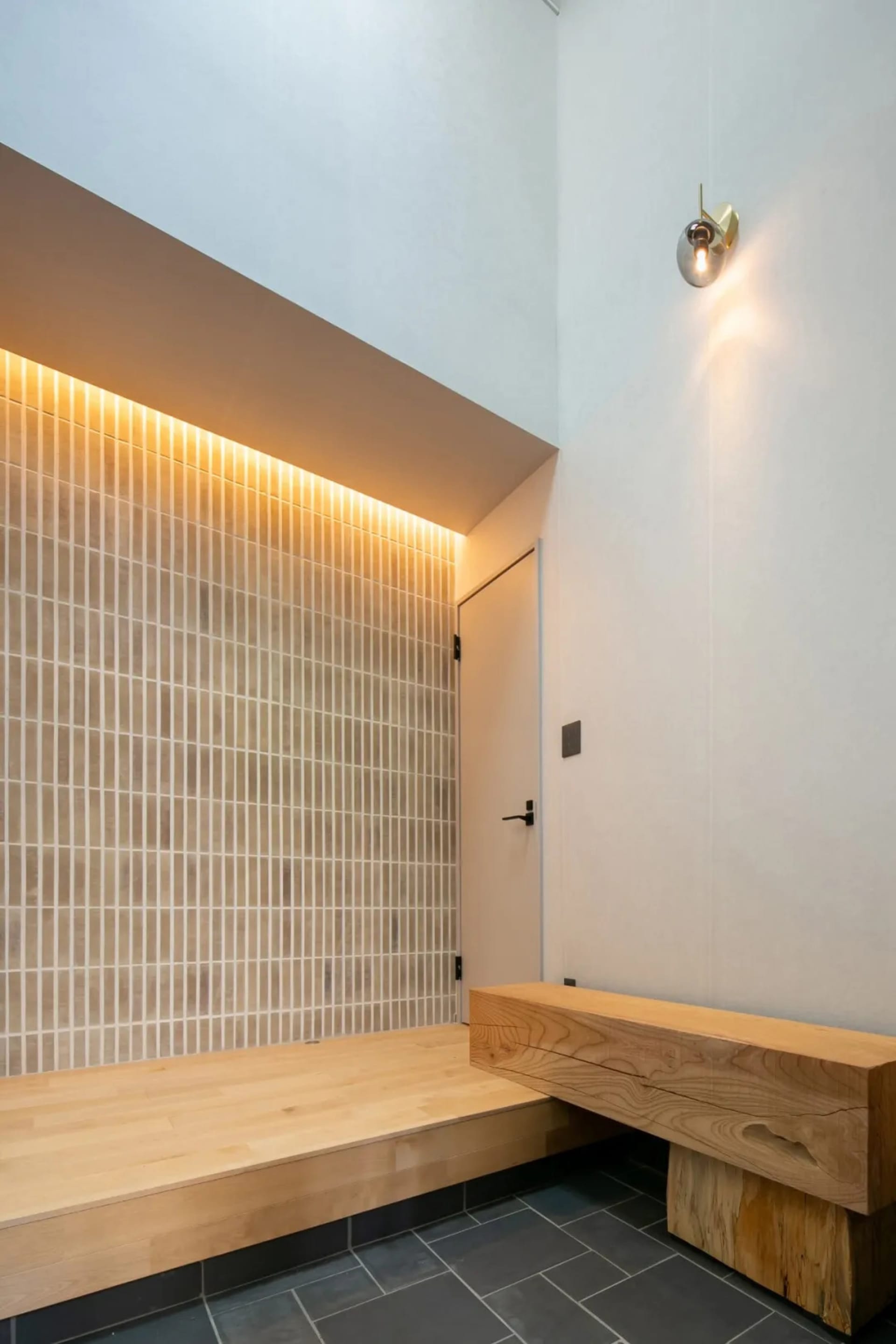 A dimly lit hallway with a wooden bench near a doorway, featuring a minimalist style with a focus on functionality and simplicity