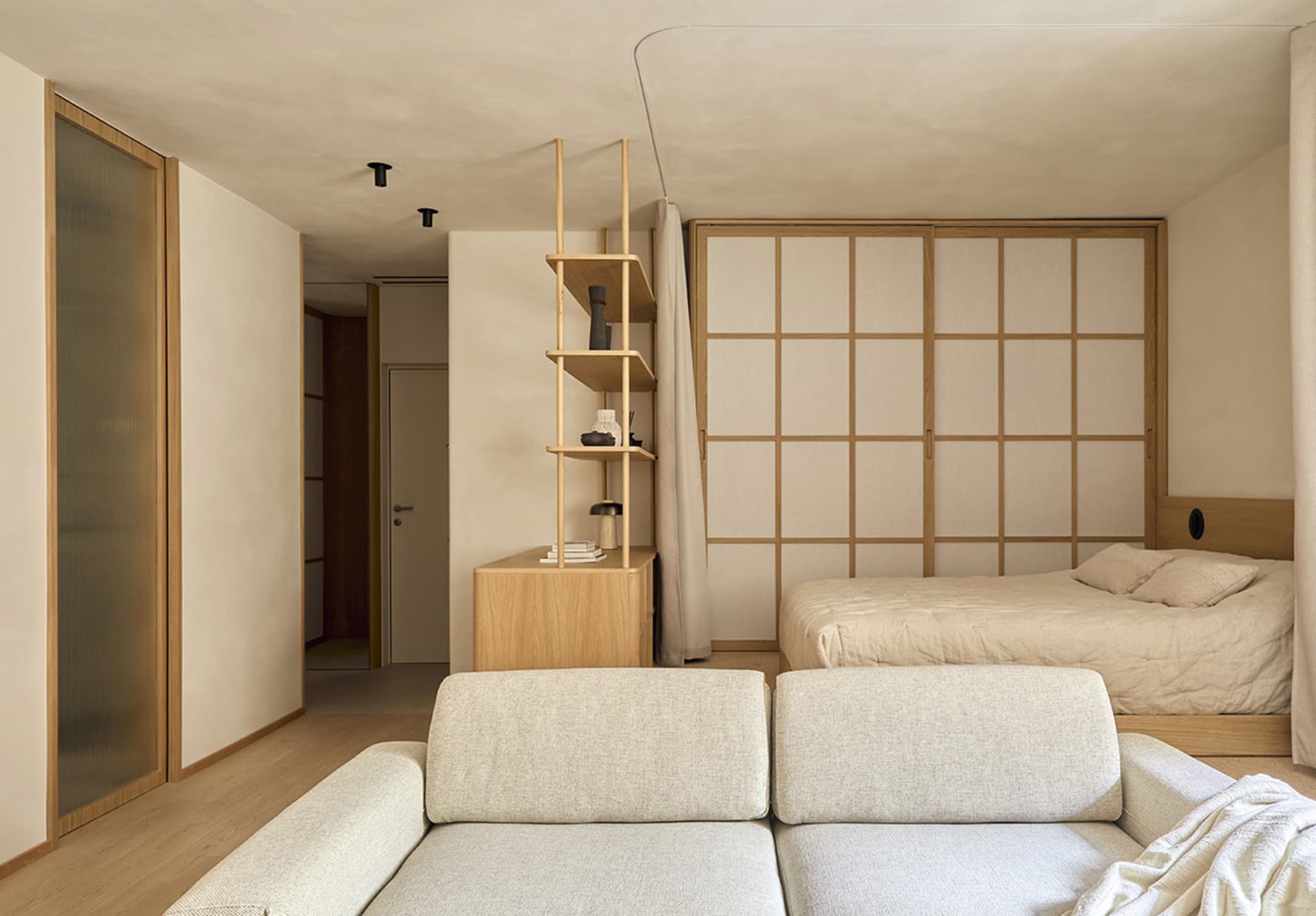 Cozy bedroom with a bed, couch, and bookshelf, featuring wood and fabric materials in a well-lit space