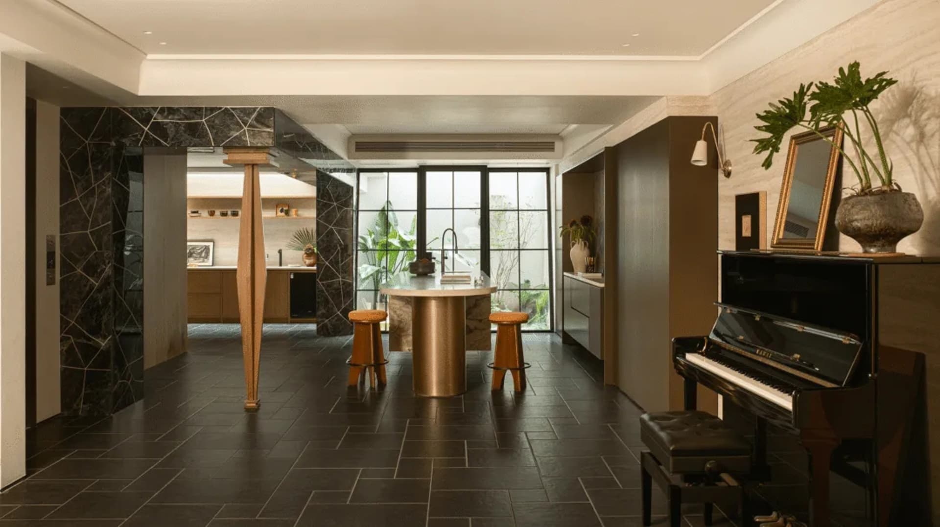 Modern kitchen and dining space with a piano, dining table, and kitchen counter, decorated with plants, vases, and bottles, illuminated by natural light