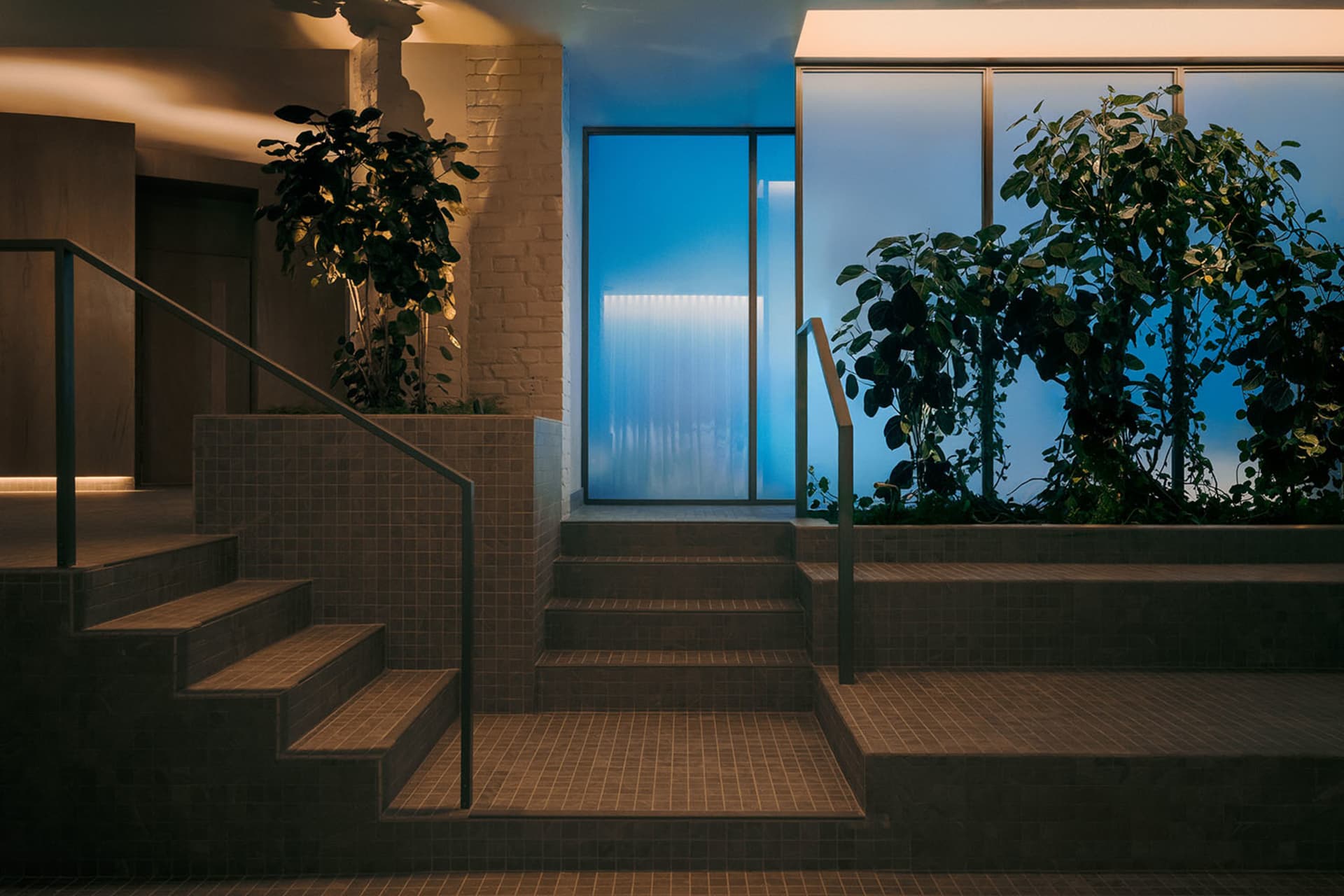 A modern stairwell with a blue staircase and railing, surrounded by plants and well-lit for a bright atmosphere