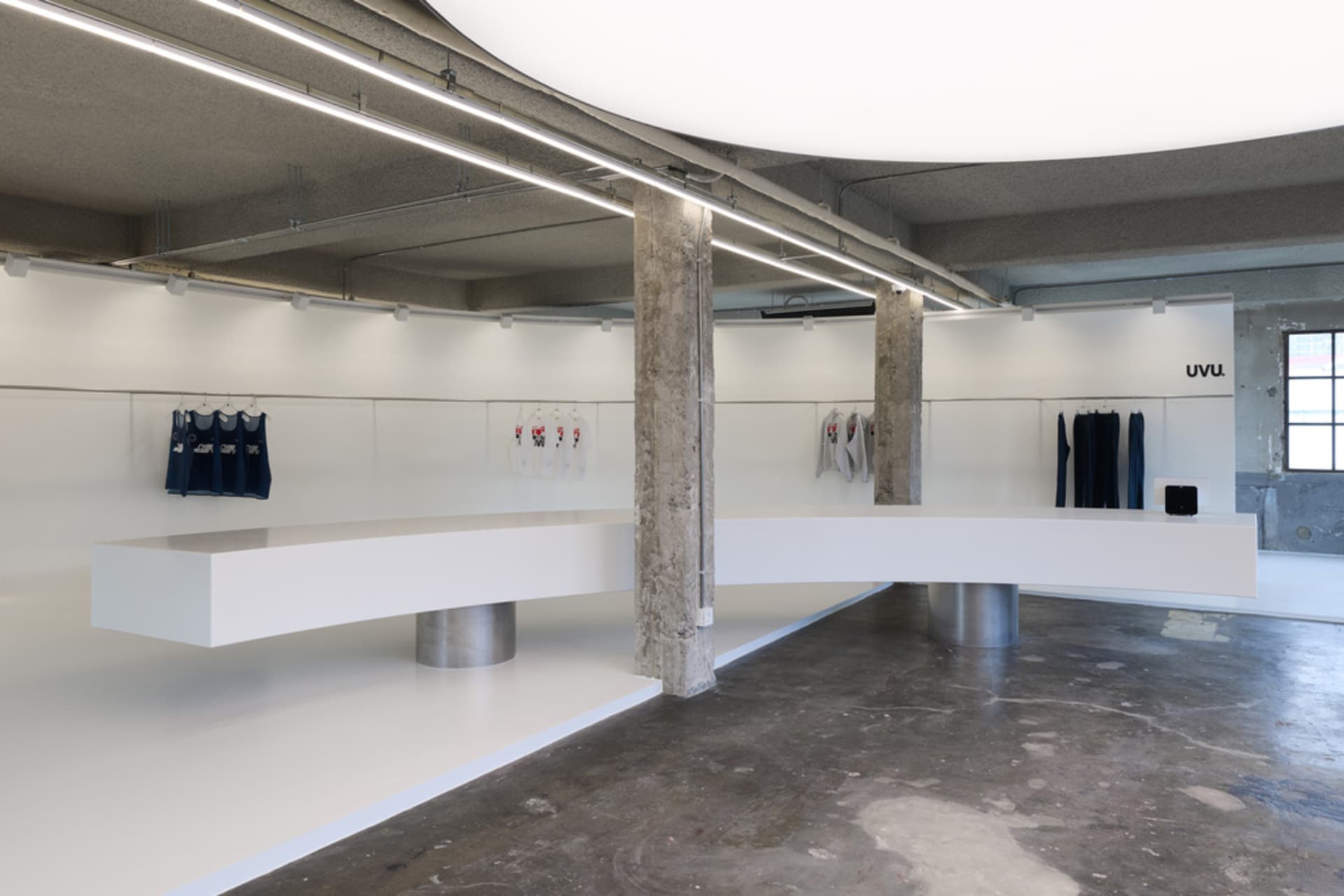 A modern retail space with a white floor and wall, featuring hanging clothes and a minimalist design
