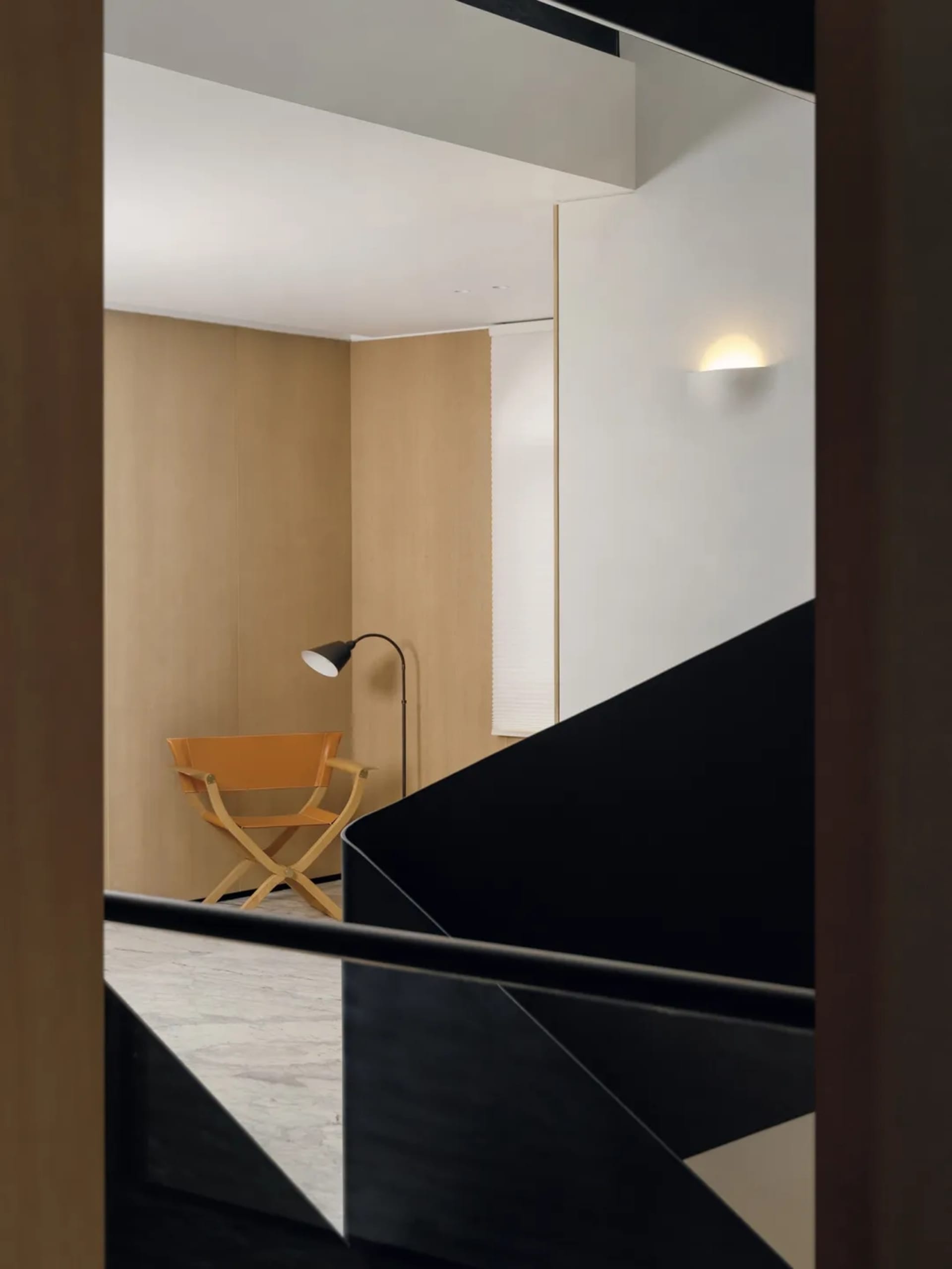Cozy living room with a wooden floor, a chair, a lamp, and a wooden staircase with a black railing