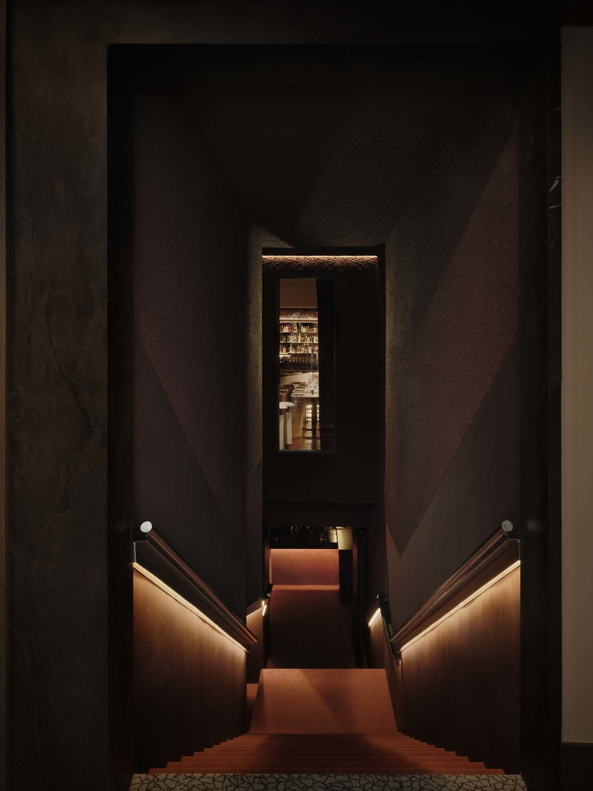 A dimly lit staircase with a red carpet and wooden steps in a quiet residential building