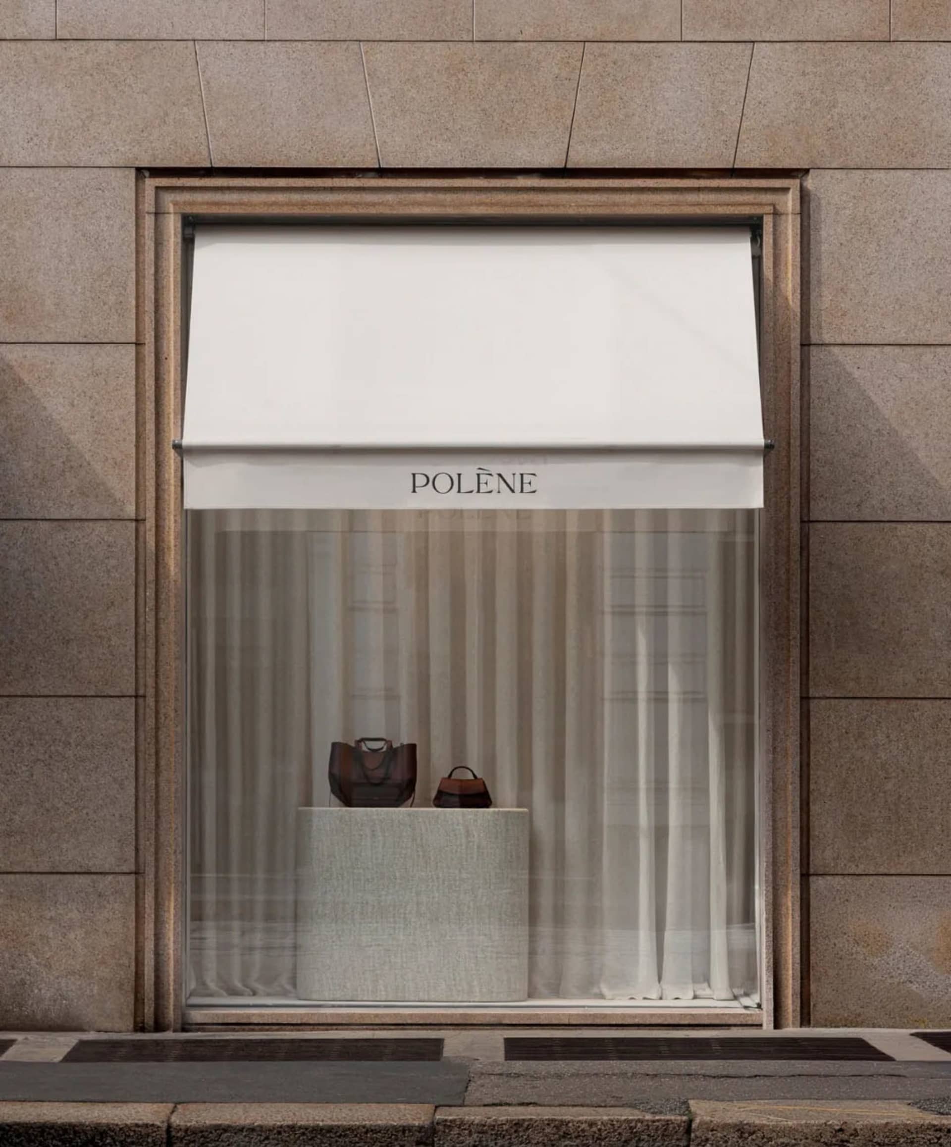 A classic storefront with a stone exterior and white display case, featuring a variety of handbags arranged in an inviting and stylish manner