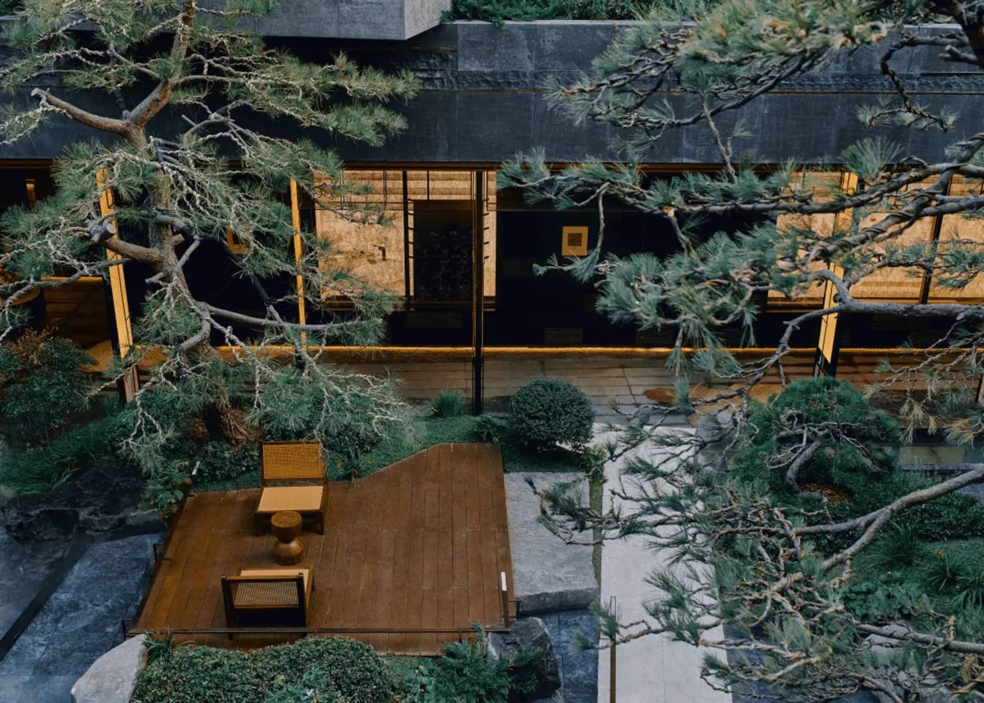 A serene outdoor space with a wooden deck surrounded by trees, a stone patio, and a stone building exterior