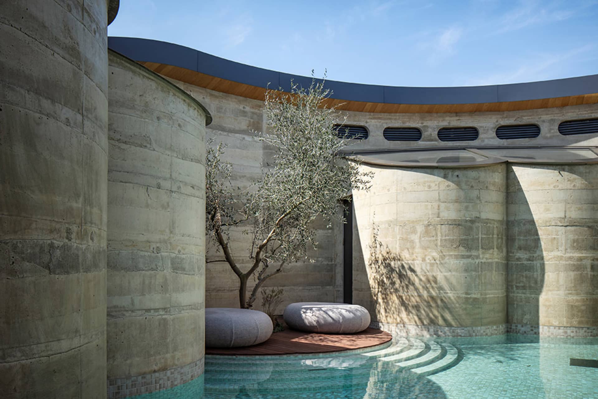 A modern outdoor space with a pool, patio, and various materials, including concrete, wood, and stone, in a well-lit and inviting atmosphere