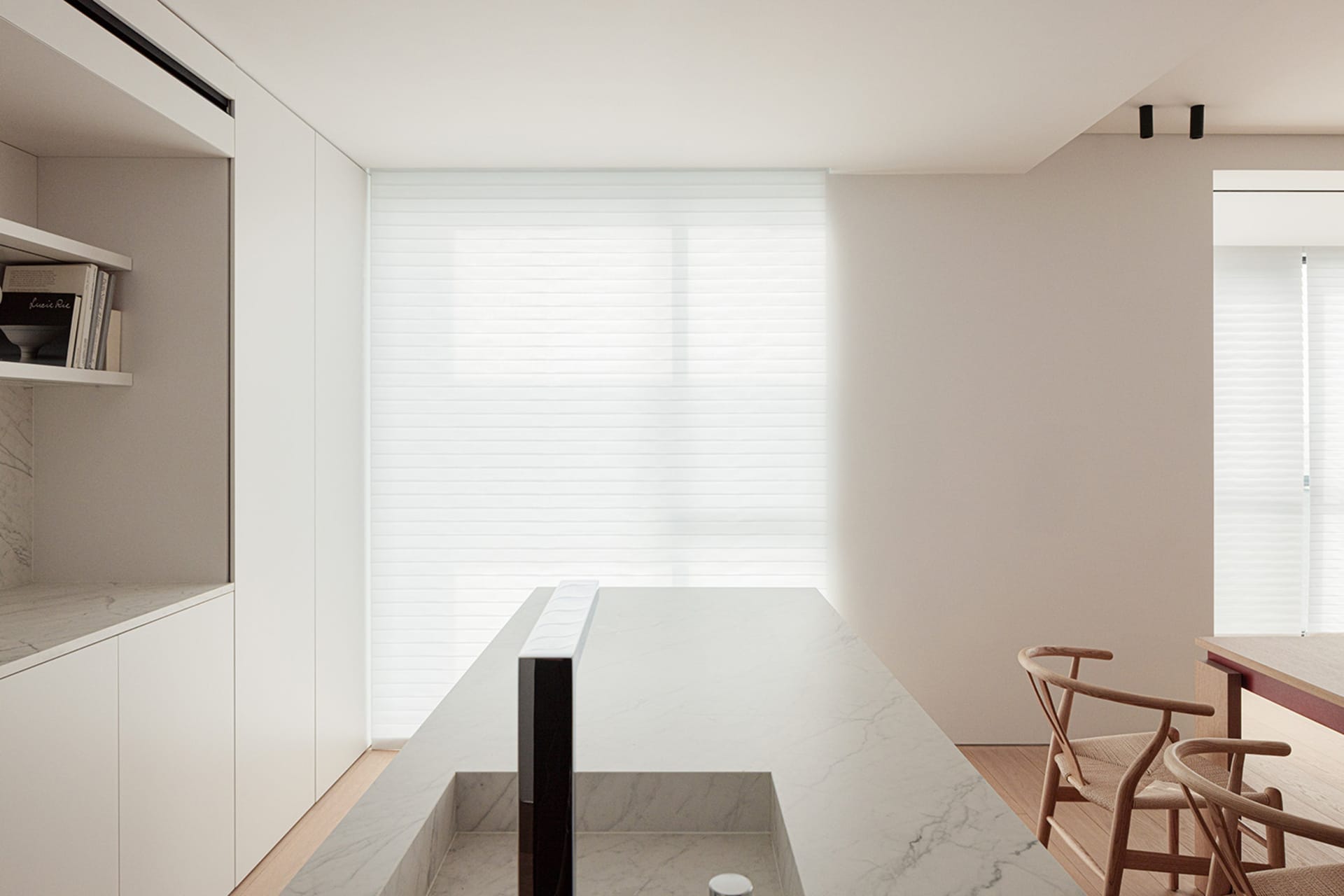 A modern kitchen with a white marble countertop, a built-in sink, a refrigerator on the left, an oven on the right, and a chair nearby, under bright lighting