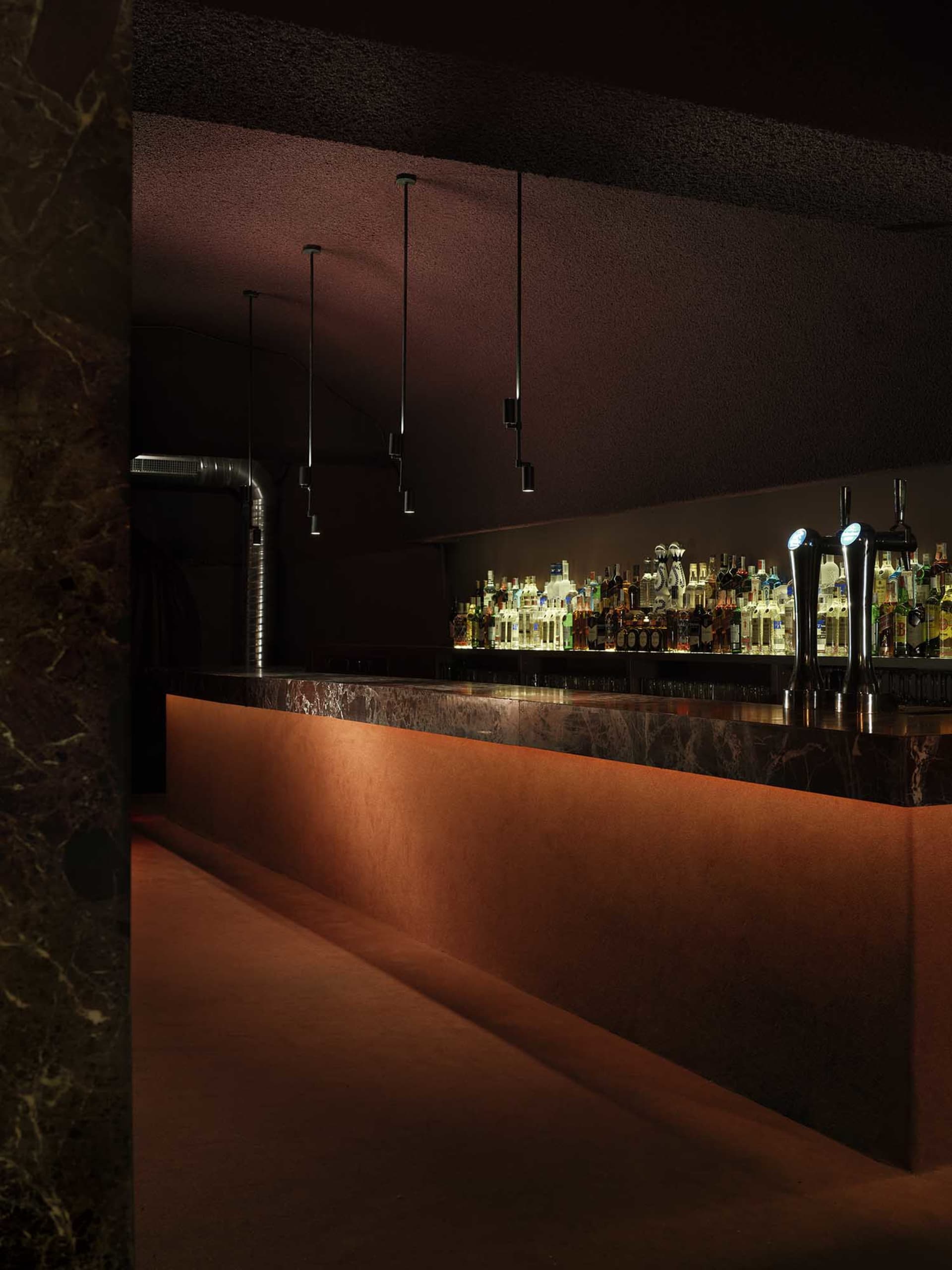 A well-lit bar with a marble countertop, bottles of various sizes arranged in a visually appealing manner, and an inviting atmosphere