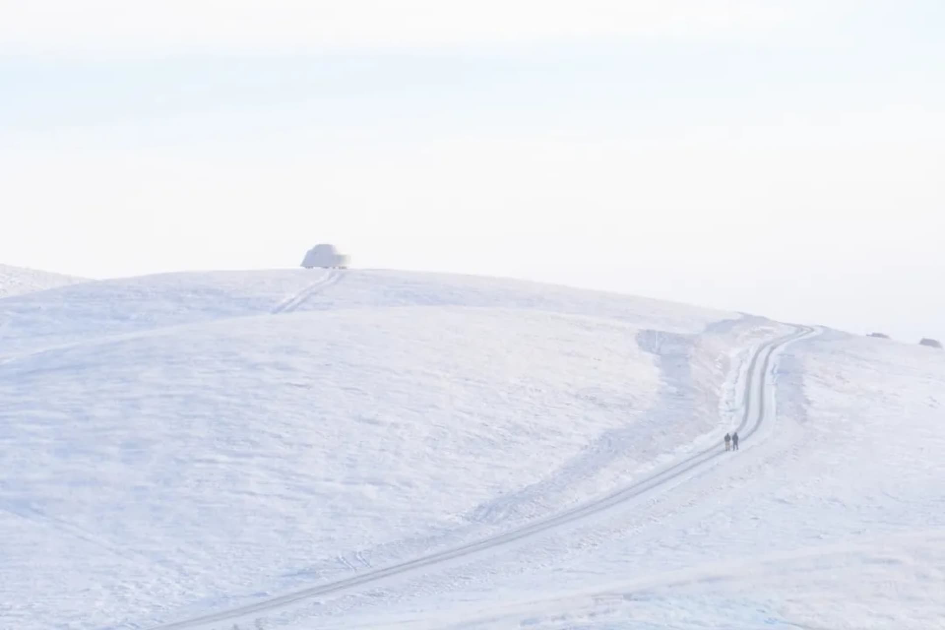 兩個走在路上的人和一輛車在遠處的雪地山路景